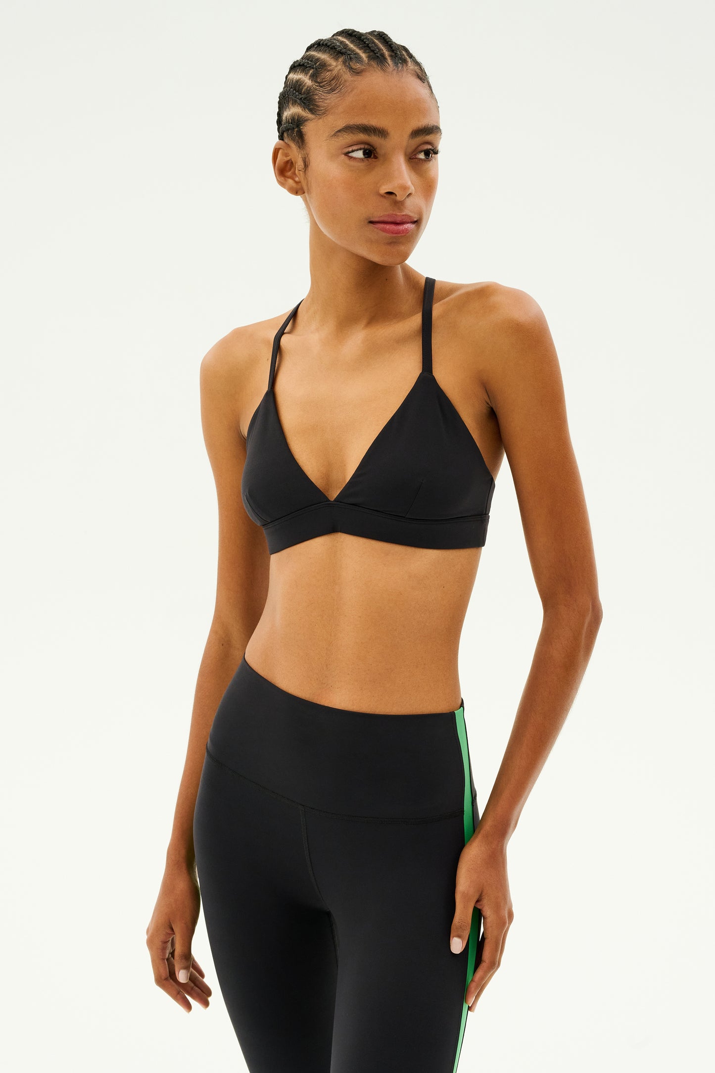 Dressed in the SPLITS59 Theo Rigor Bra - Black, this individual exudes confidence against a plain backdrop while wearing black leggings with a bold green stripe, perfectly equipped for multi-sport performance.