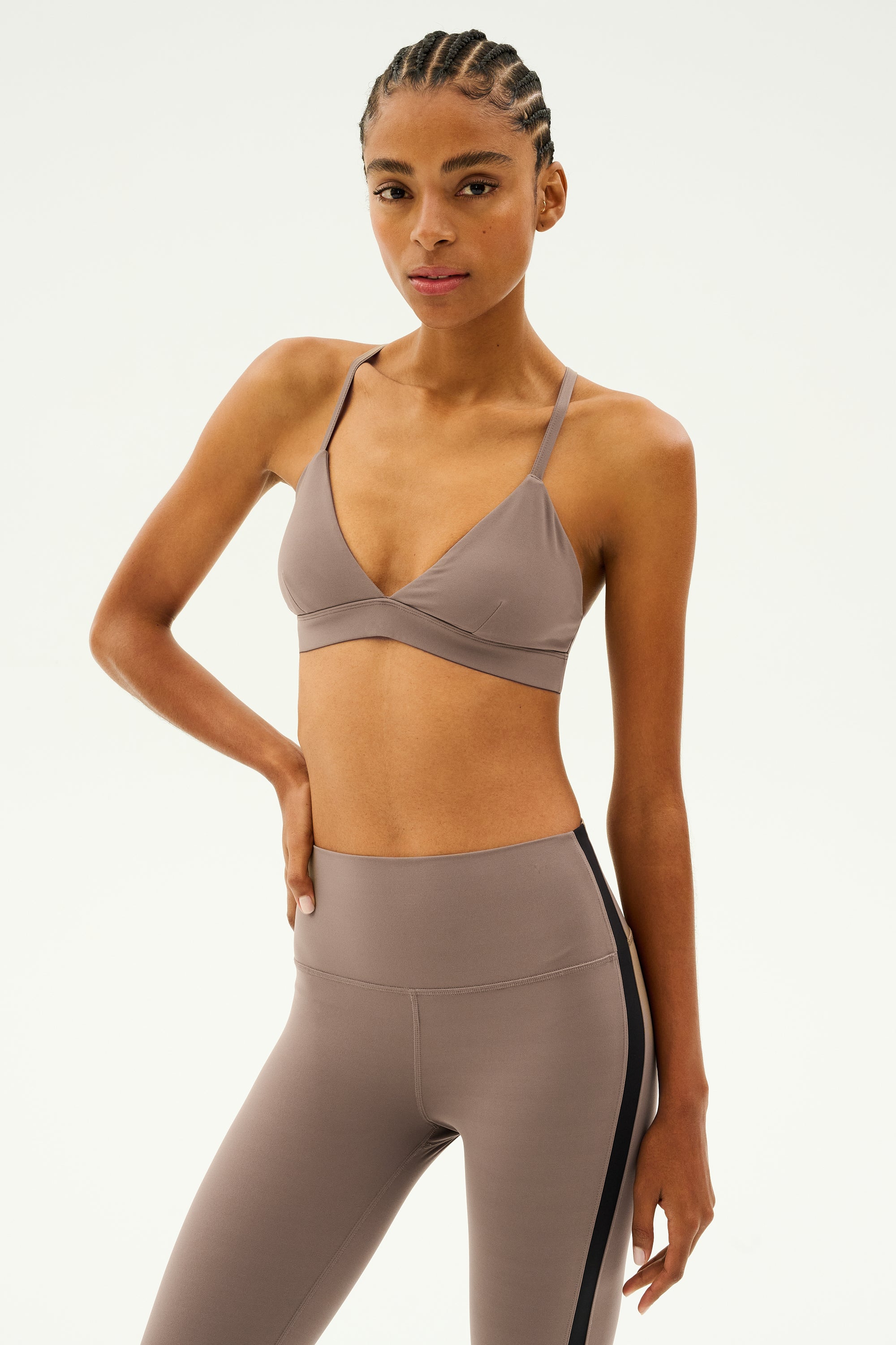 A person wearing a Lentil Theo Rigor Bra by SPLITS59, paired with leggings, stands with one hand on their hip, flaunting an ultra-luxe look ideal for multi-sport performance.