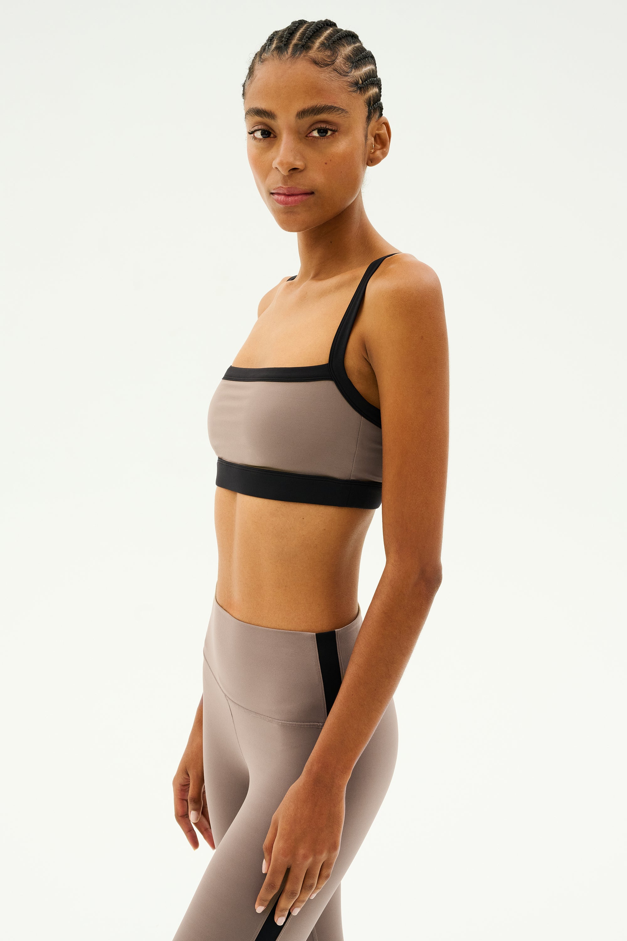 A person wearing a Lentil/Black Monah Rigor Bra by SPLITS59 stands against a plain background, ready for intense gym workouts.