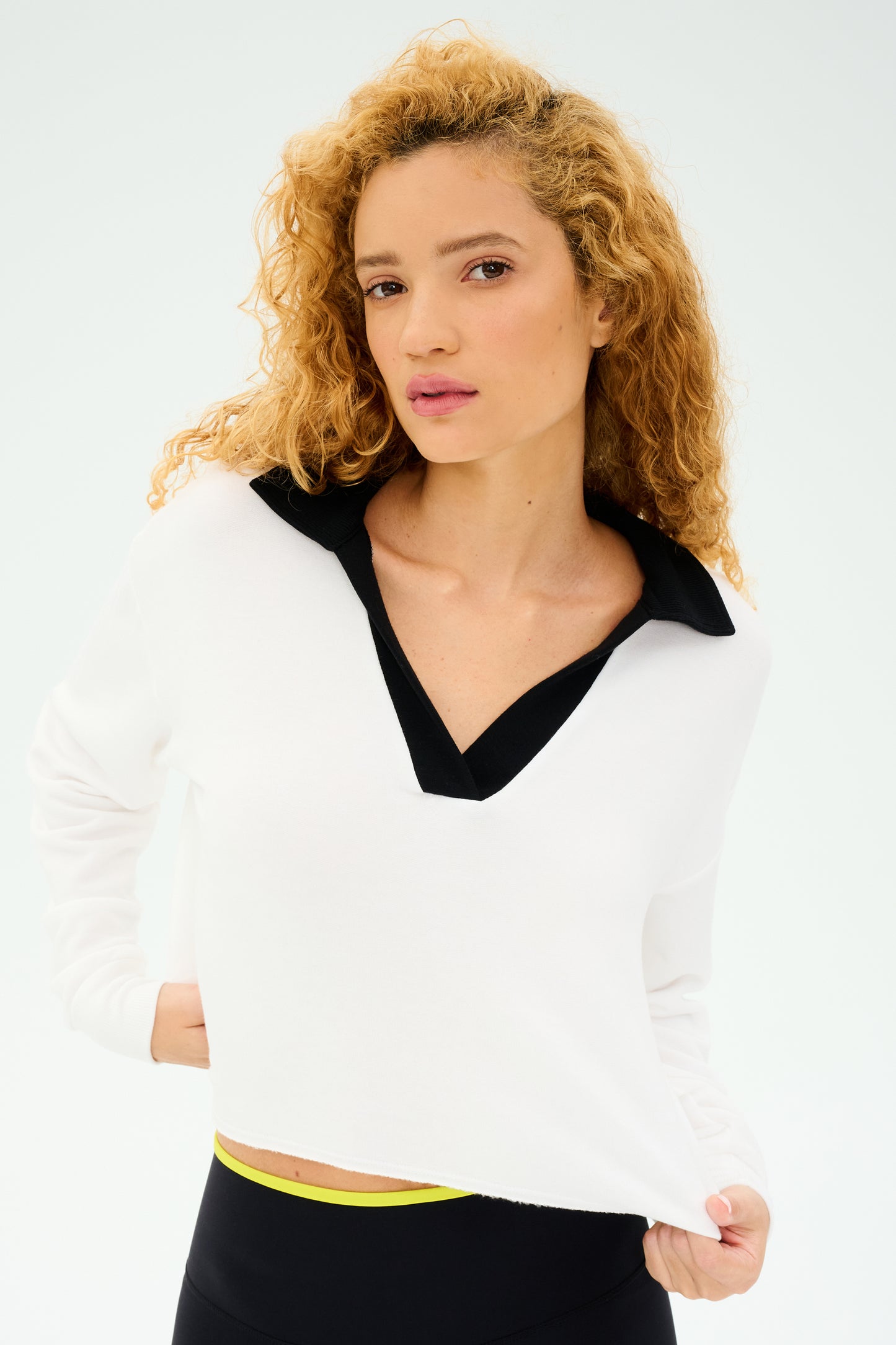 A person with curly hair wears the Joan Fleece Polo Sweatshirt by SPLITS59, featuring a white body and black collar, resembling a rugby polo, against a plain background.