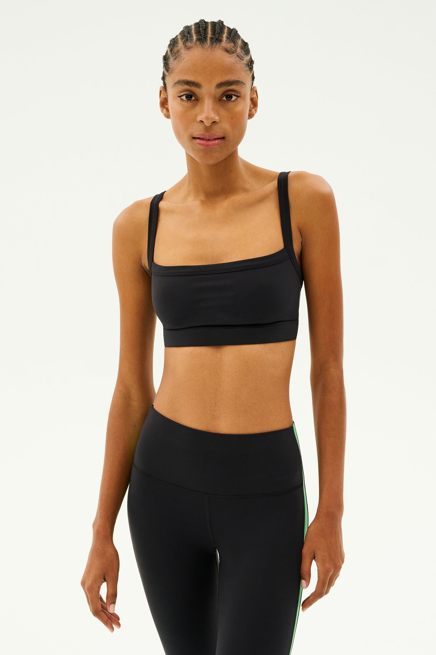 A person is displaying the SPLITS59 Monah Rigor Bra - Black teamed with sleek black leggings, set against a plain background—ideal attire for intense gym workouts.