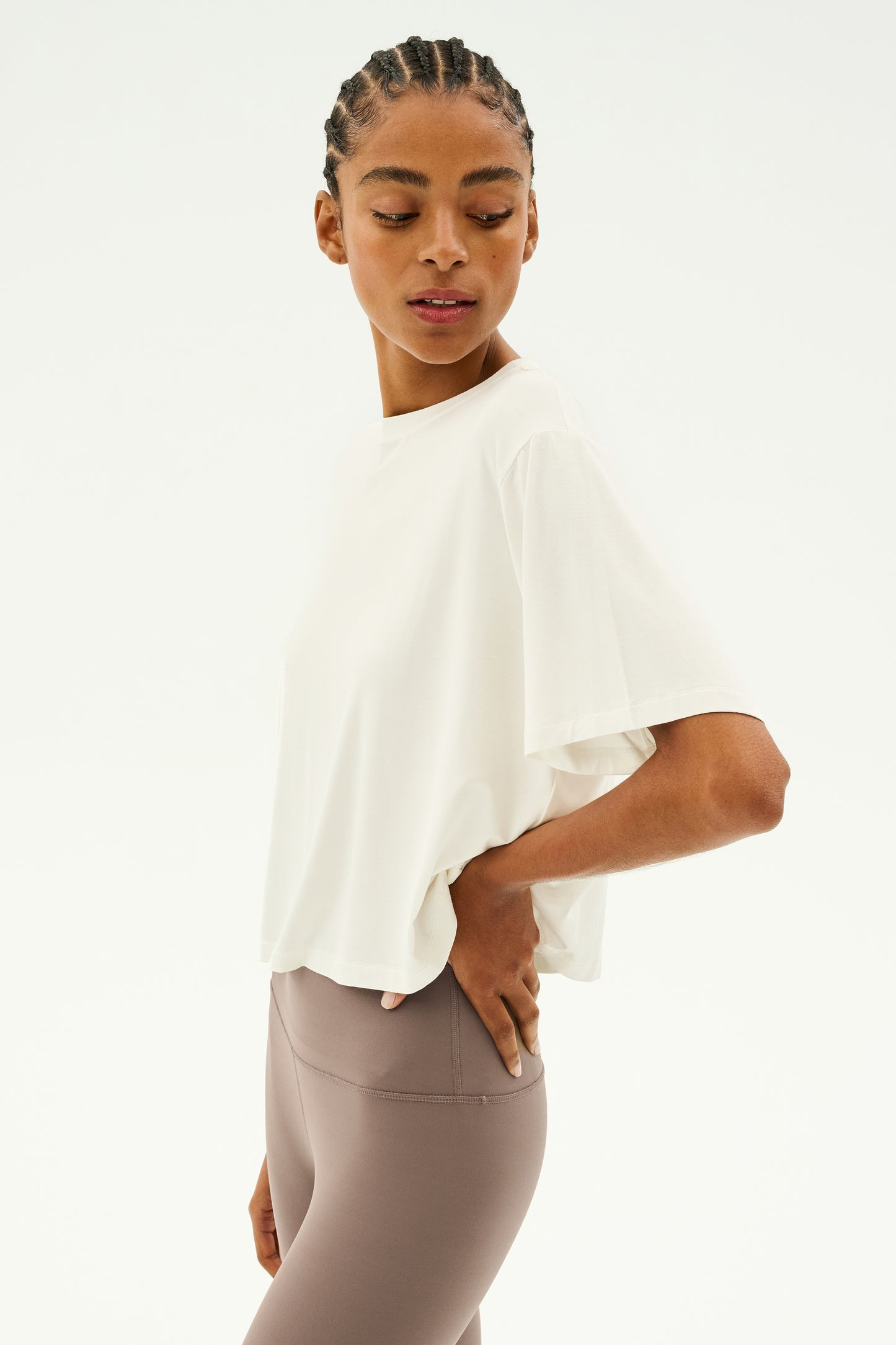 A person wearing a white Djuna Oversized Jersey Tee by SPLITS59 and taupe leggings against a plain background, posing with one hand on their hip.