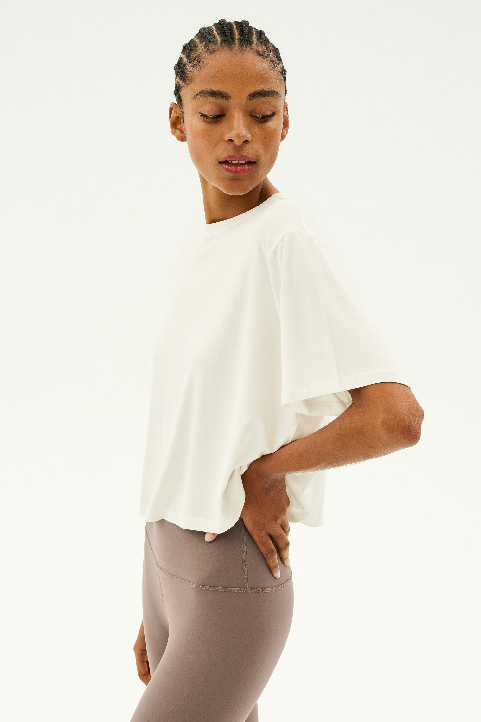 A person wearing a white Djuna Oversized Jersey Tee by SPLITS59 and taupe leggings against a plain background, posing with one hand on their hip.