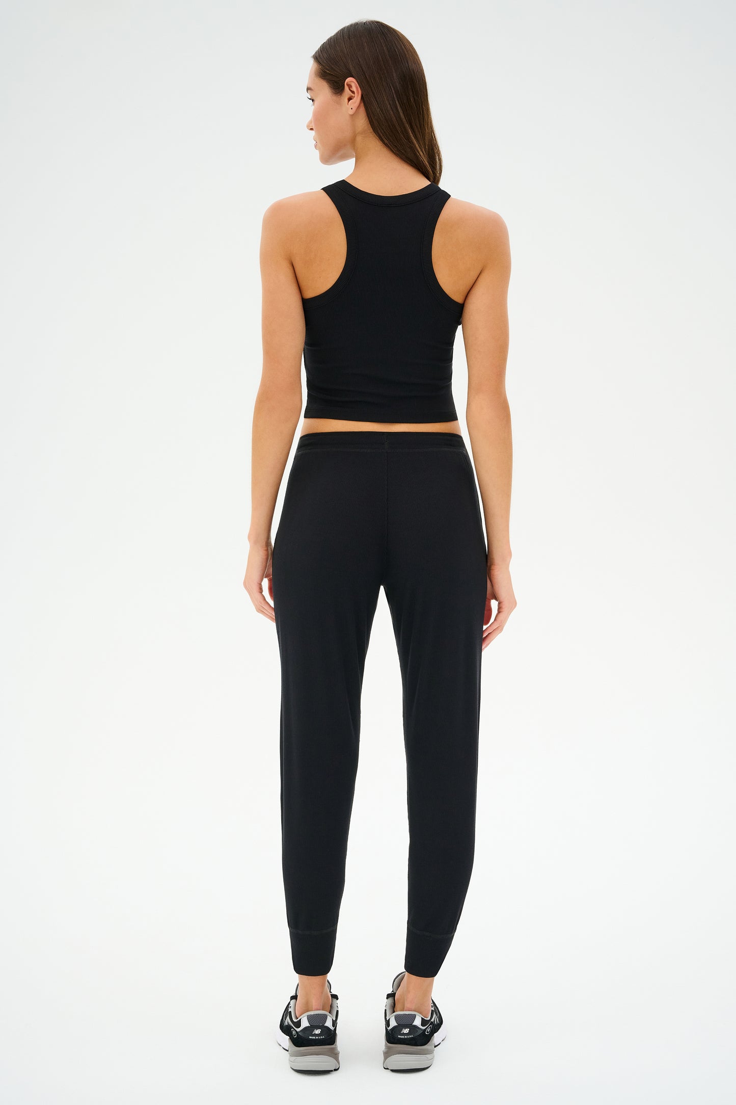 A person in a black SPLITS59 Kiki Rib 7/8 Sweatpant stands with their back to the camera against a white background, highlighting the elegant casualness of these MADE IN LOS ANGELES lounge pants.