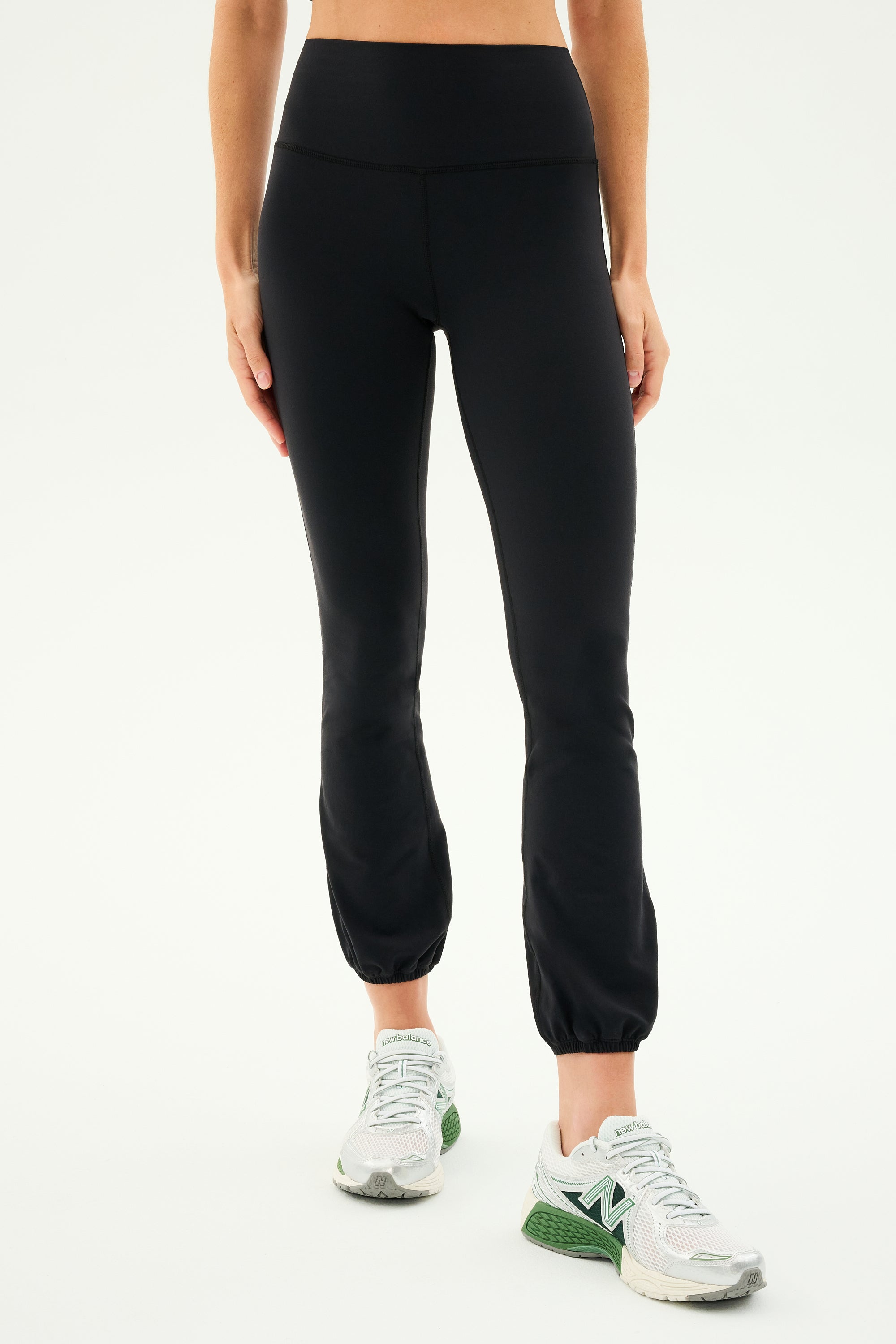 A person wearing SPLITS59 Icon High Waist Supplex Legging - Black and white running shoes stands against a plain background.