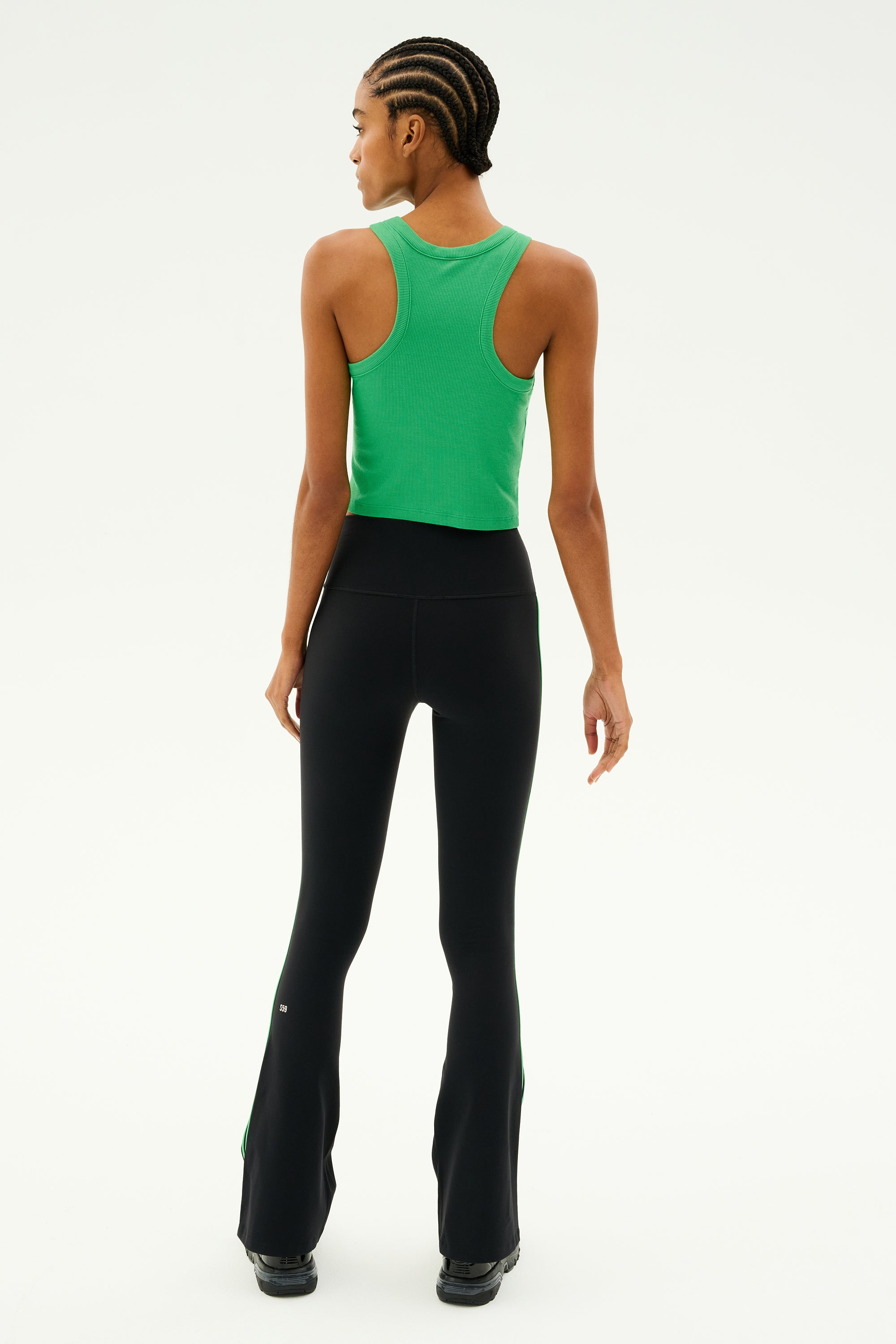 A person wearing the SPLITS59 Kiki Rib Crop in Grass paired with black leggings stands with their back turned, highlighting the exquisite craftsmanship of baby rib fabric. This MADE IN LOS ANGELES design flawlessly combines style and comfort in every thread.