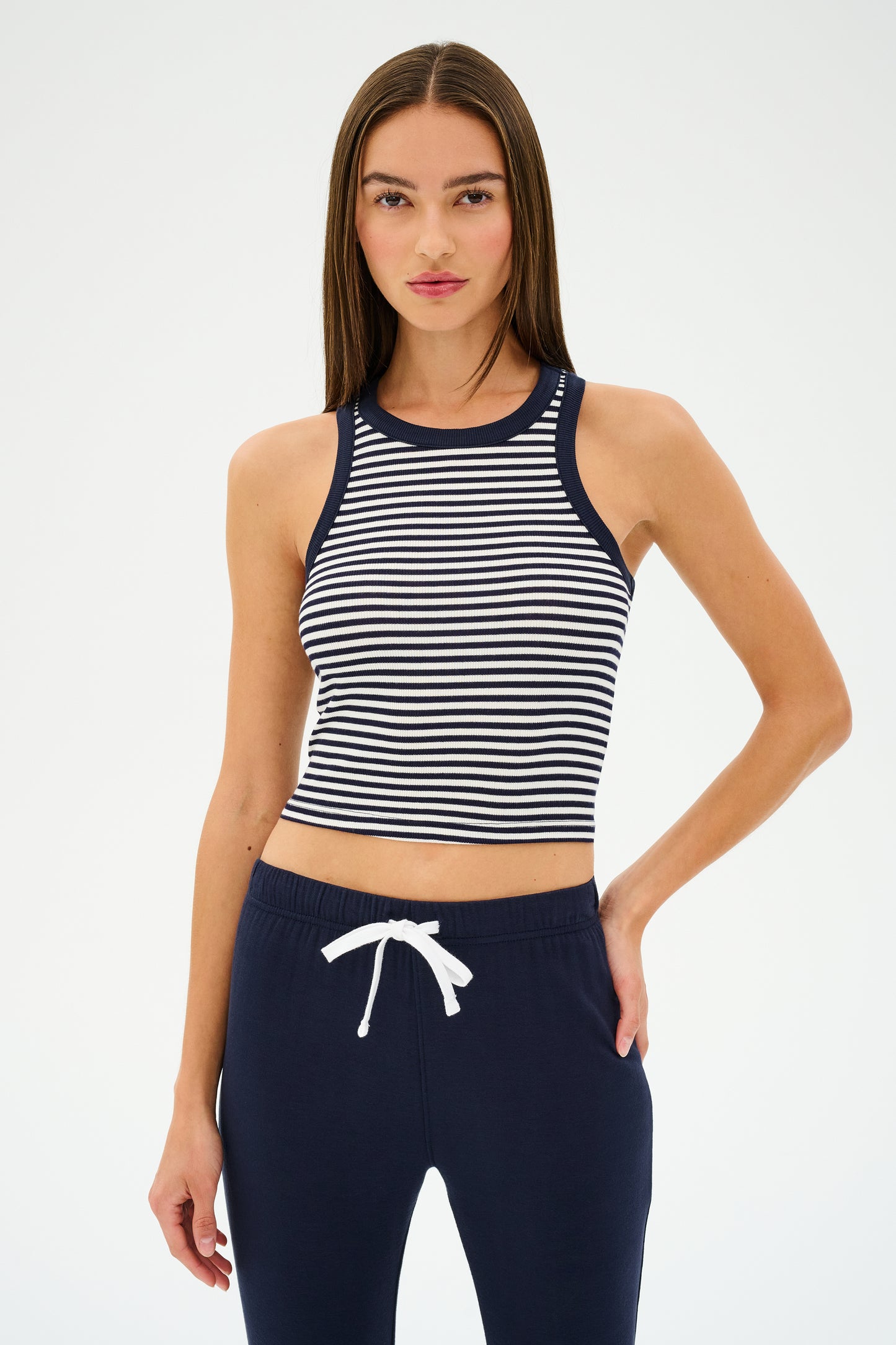 A person dons the SPLITS59 Kiki Rib Crop Tank in White/Indigo Stripe, crafted from soft baby rib fabric, paired with navy pants against a plain background. Made in Los Angeles, this outfit exudes effortless style.