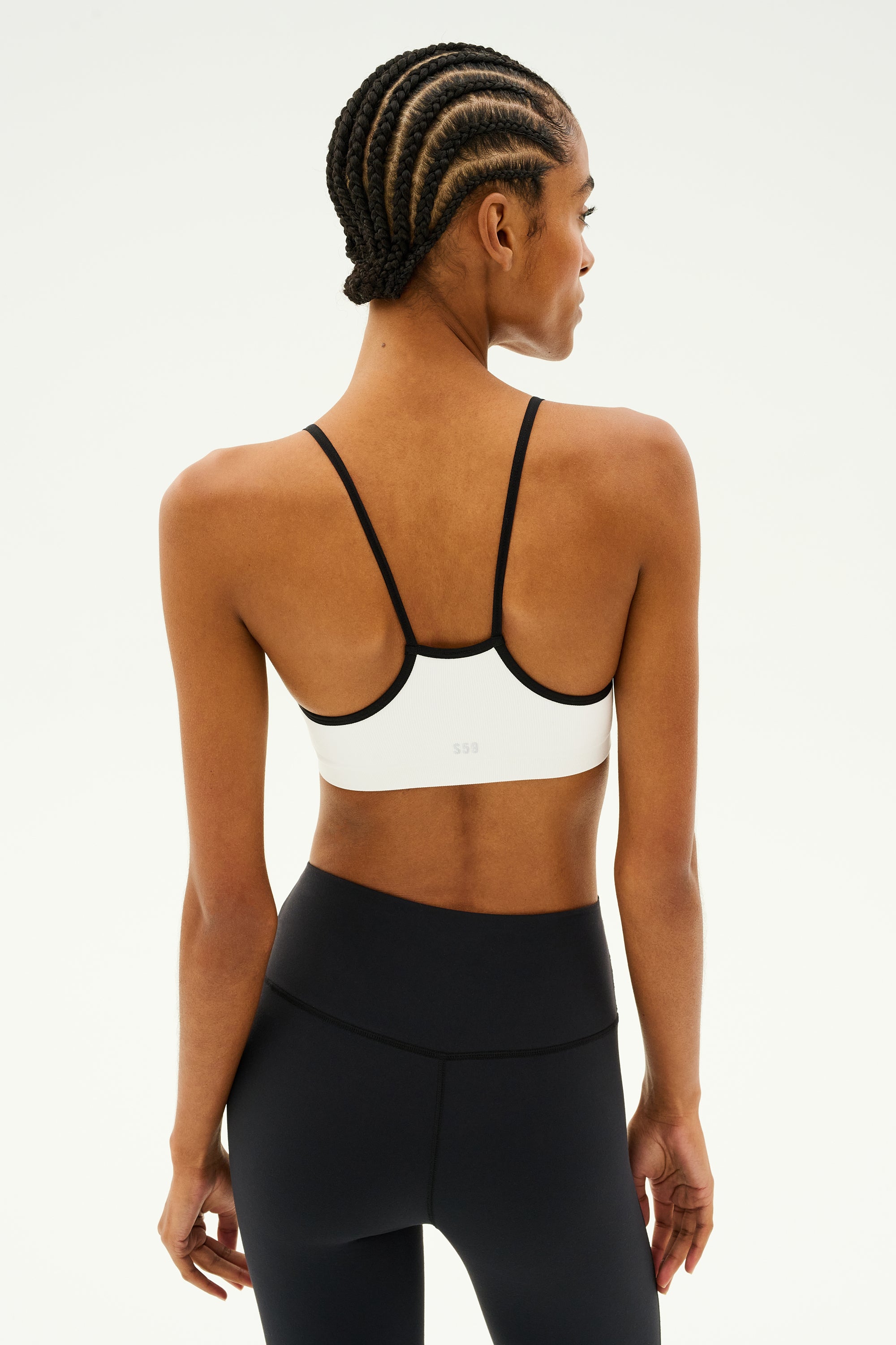 A person with braided hair is wearing a SPLITS59 Loren Seamless Bra in White/Black and black leggings, ideal for gym workouts, standing against a neutral background.