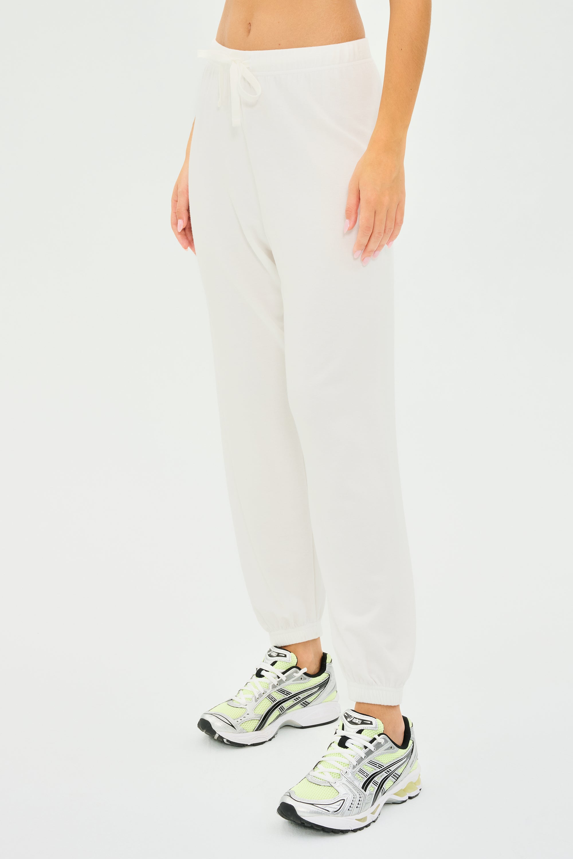 Wearing the Andie Oversized Fleece Sweatpant - White by SPLITS59 and white sneakers with green accents, someone prepares for a cool weather workout against a plain white backdrop.