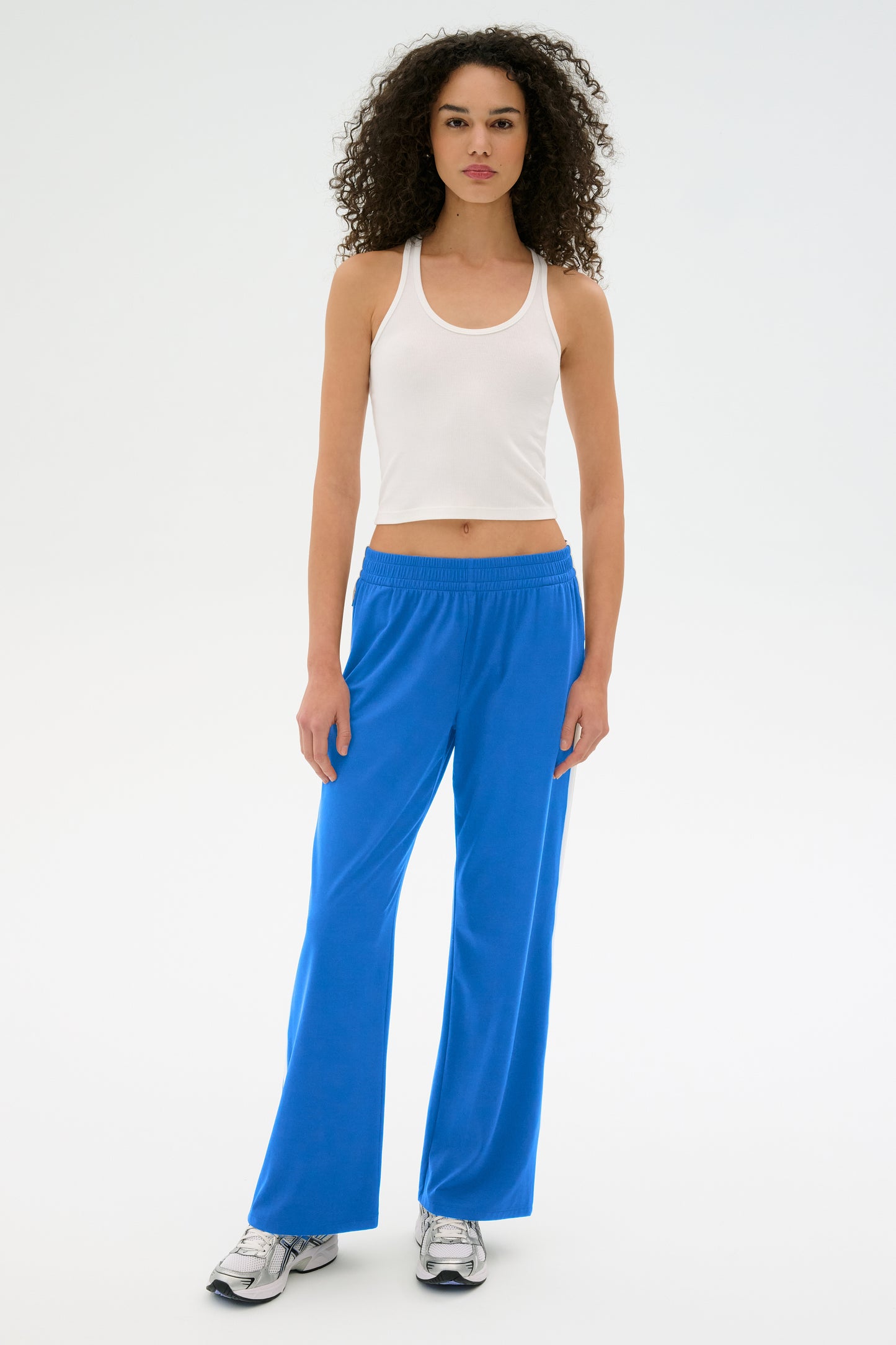 A person in a white tank top and SPLITS59's Maxie Rigor Track Pant - Classic Blue/White with sneakers stands against a white background.