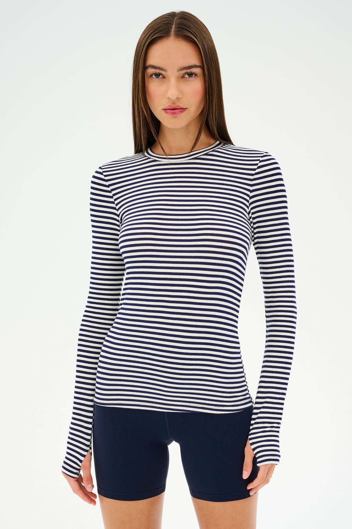 A person wearing a SPLITS59 Louise Rib Long Sleeve in White/Indigo Stripe and dark shorts stands against a plain background.