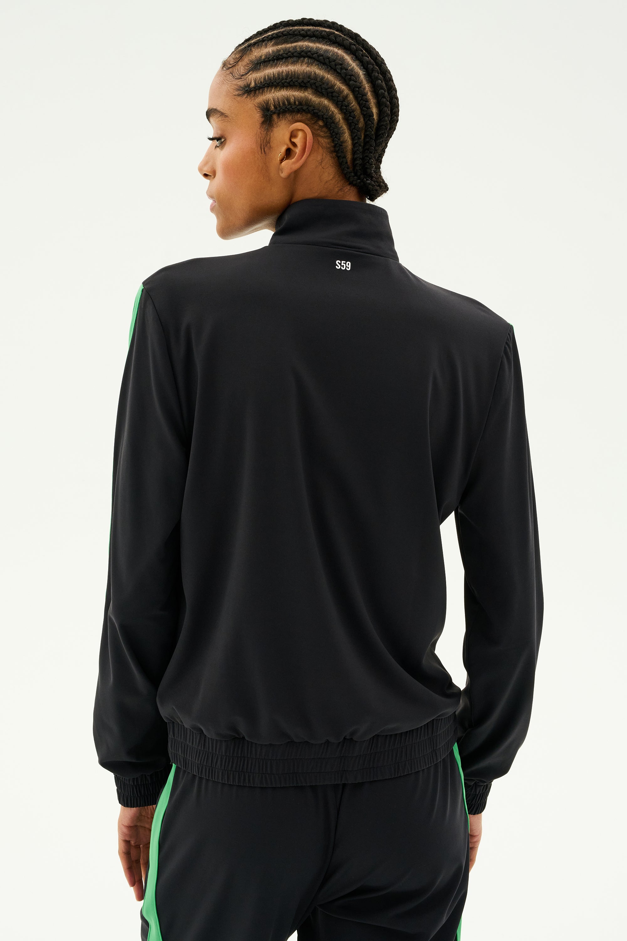 A person with braided hair sports the SPLITS59 Max Rigor Track Jacket in black, featuring grass-colored stripes, as they are viewed from the back against a plain background.