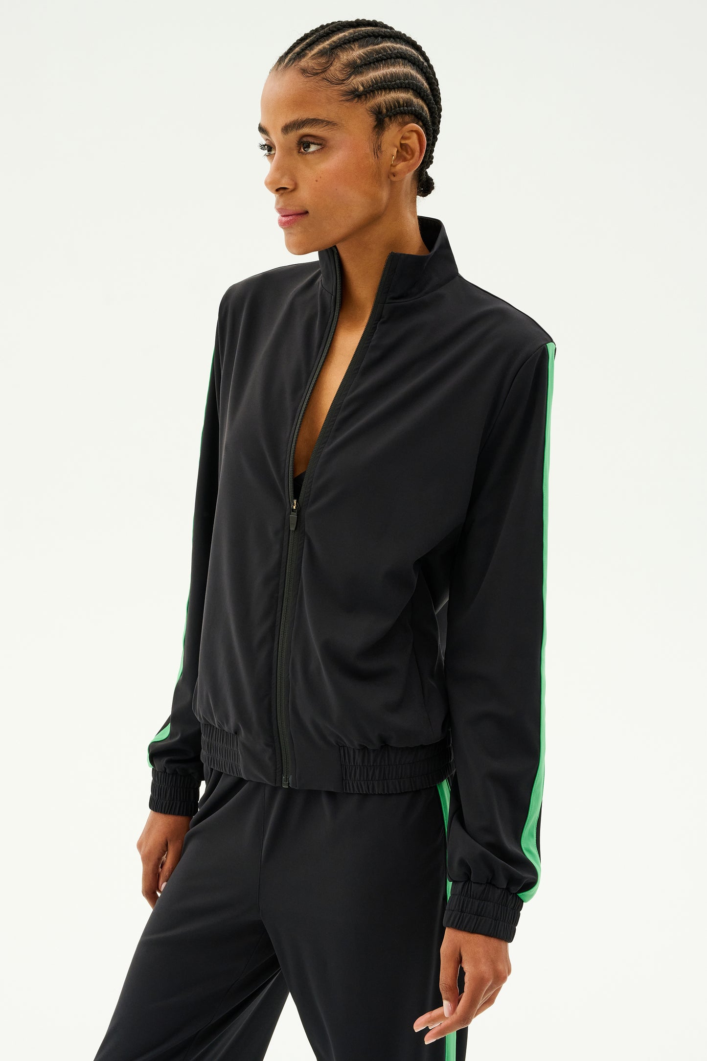 A person wearing the SPLITS59 Max Rigor Track Jacket in Black/Grass is looking to the side against a plain background.