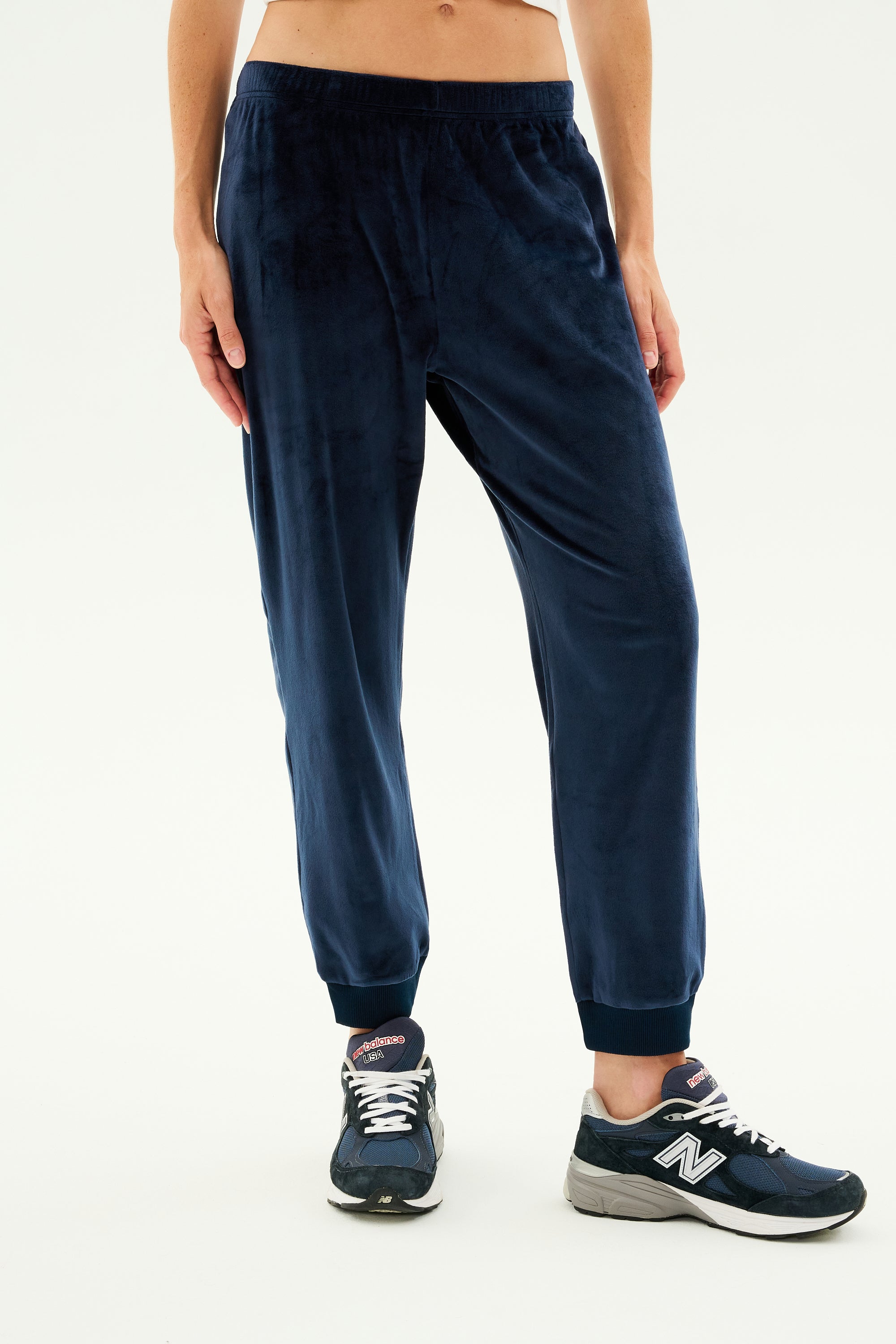 Person modeling indigo Rhys Velour Jogger pants by SPLITS59 and black New Balance sneakers, perfect for lounging. The background is plain white.