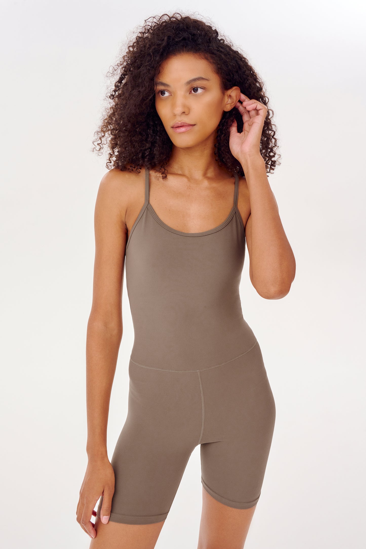 The model is wearing a brown Airweight 6" Short Jumpsuit designed for hot yoga, made by SPLITS59.