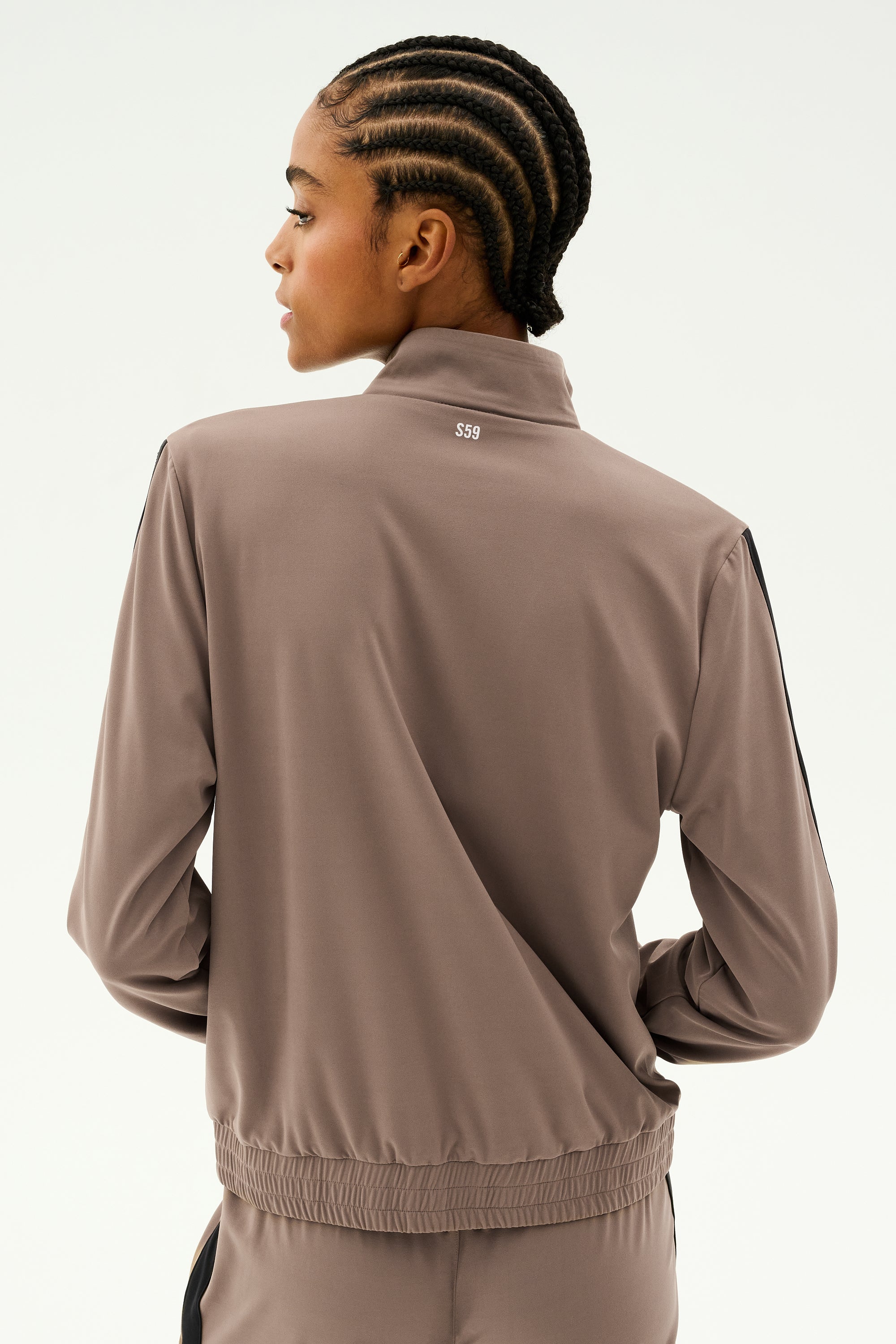 Seen from the back, a person with braided hair is wearing a taupe Max Rigor Track Jacket in Lentil/Black by SPLITS59, paired with matching Max Rigor Track Pants, set against a plain background.