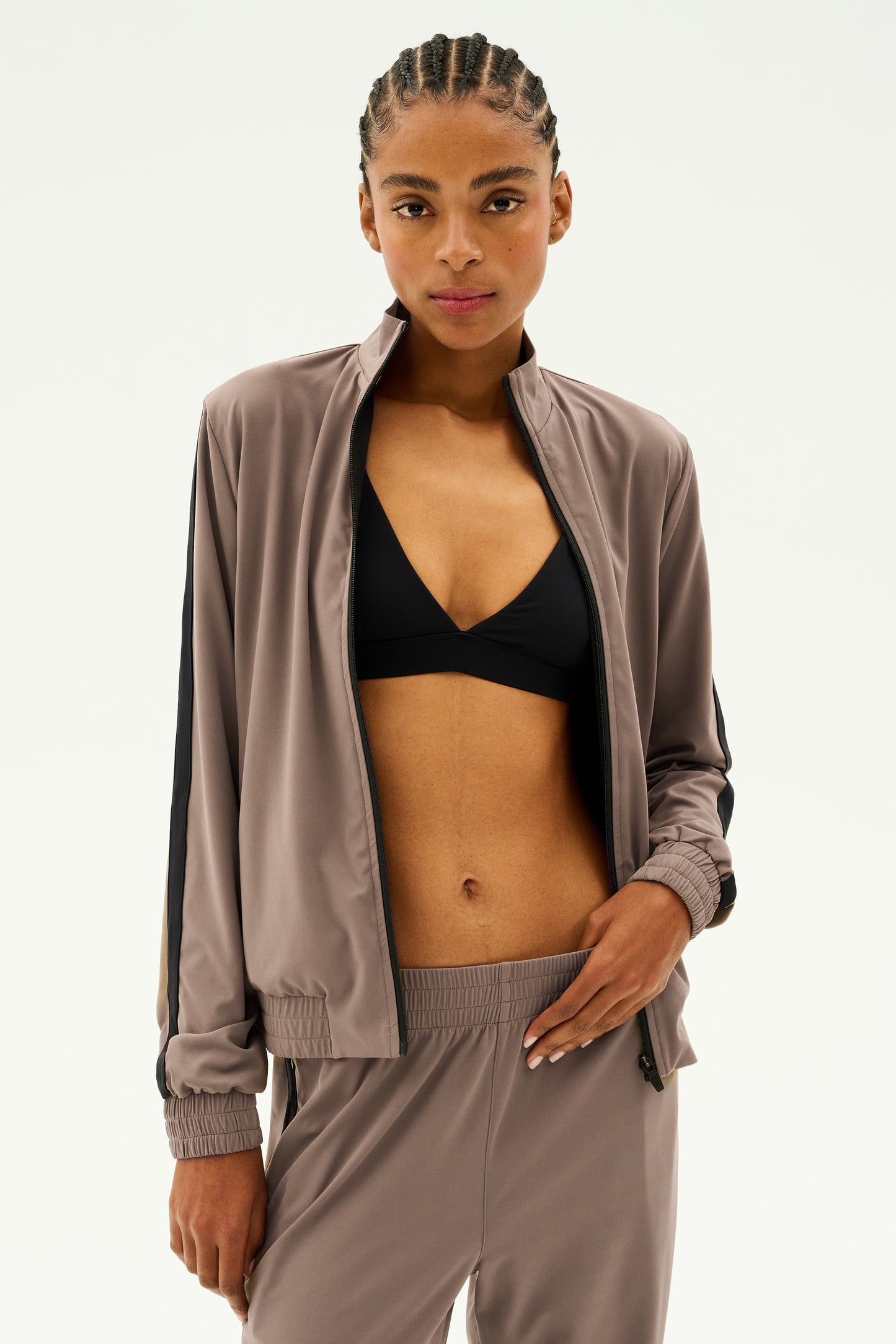 A person wearing the Max Rigor Track Jacket in Lentil/Black from SPLITS59, paired with matching pants made from Rigor fabric, over a black sports bra, stands against a plain white background.