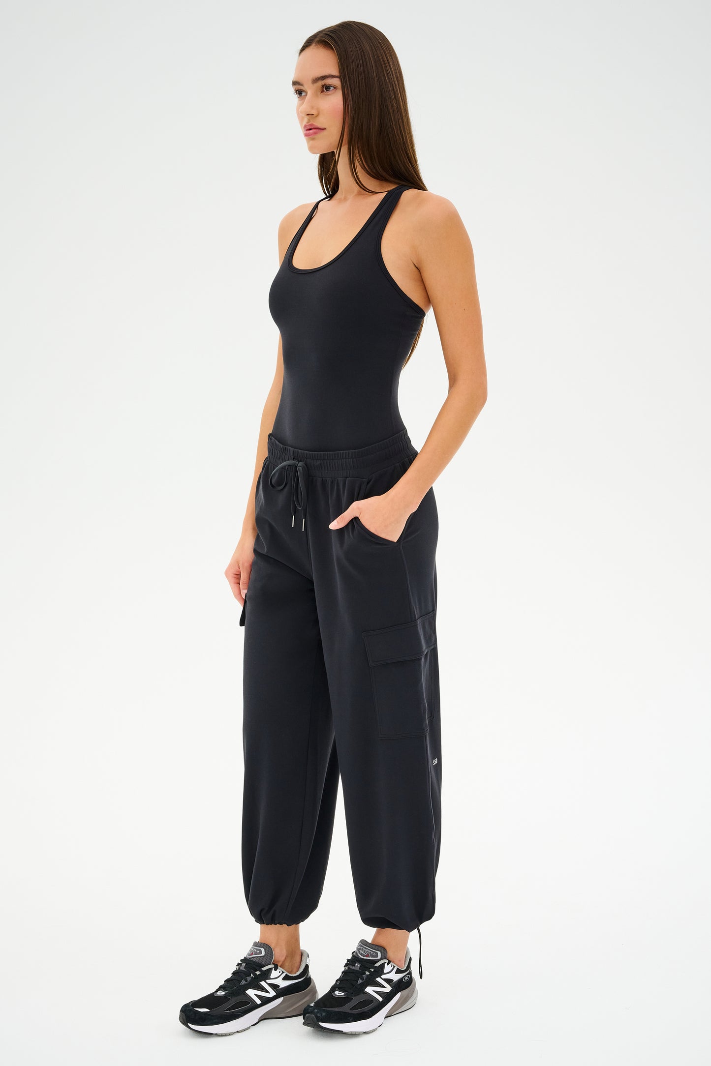 A person wearing a black tank top paired with SPLITS59's Nico Airweight Cargo Pant in black and black sneakers stands against a plain background.