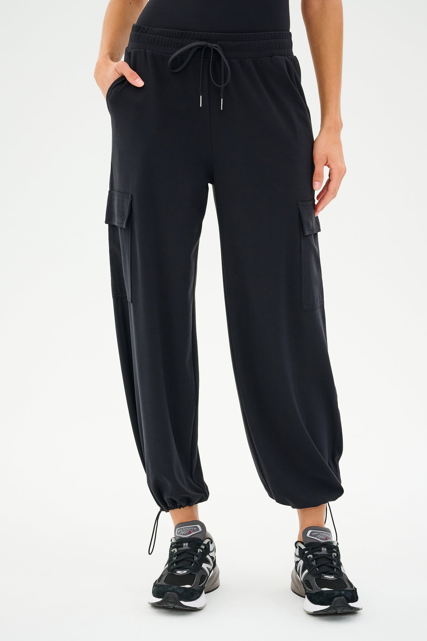 A person dressed in SPLITS59's Nico Airweight Cargo Pant - Black, featuring a relaxed fit and drawstring waist paired with sneakers.