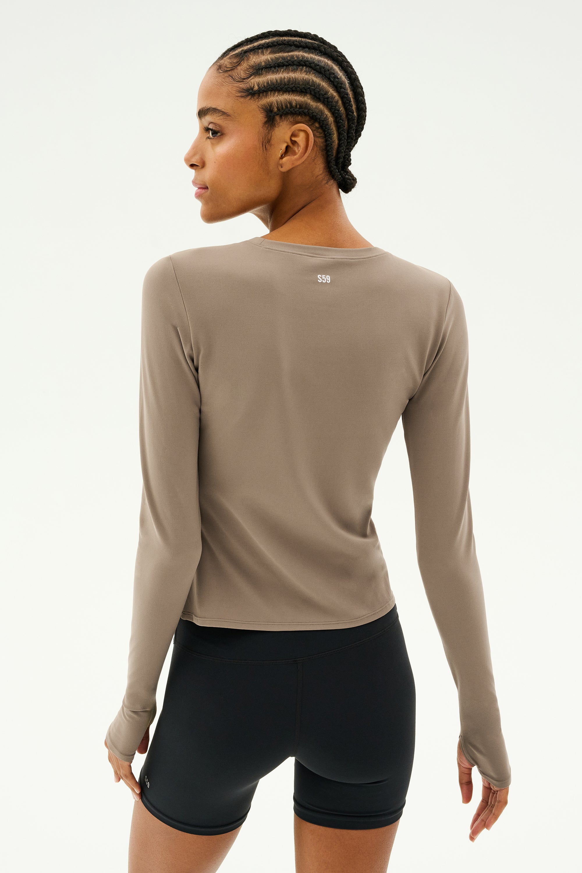 An individual with cornrows is wearing the SPLITS59 Airweight Lite LS Waist Length top in Lentil and black shorts, designed with quick-dry fabric, facing away in a neutral pose ideal for gym workouts.