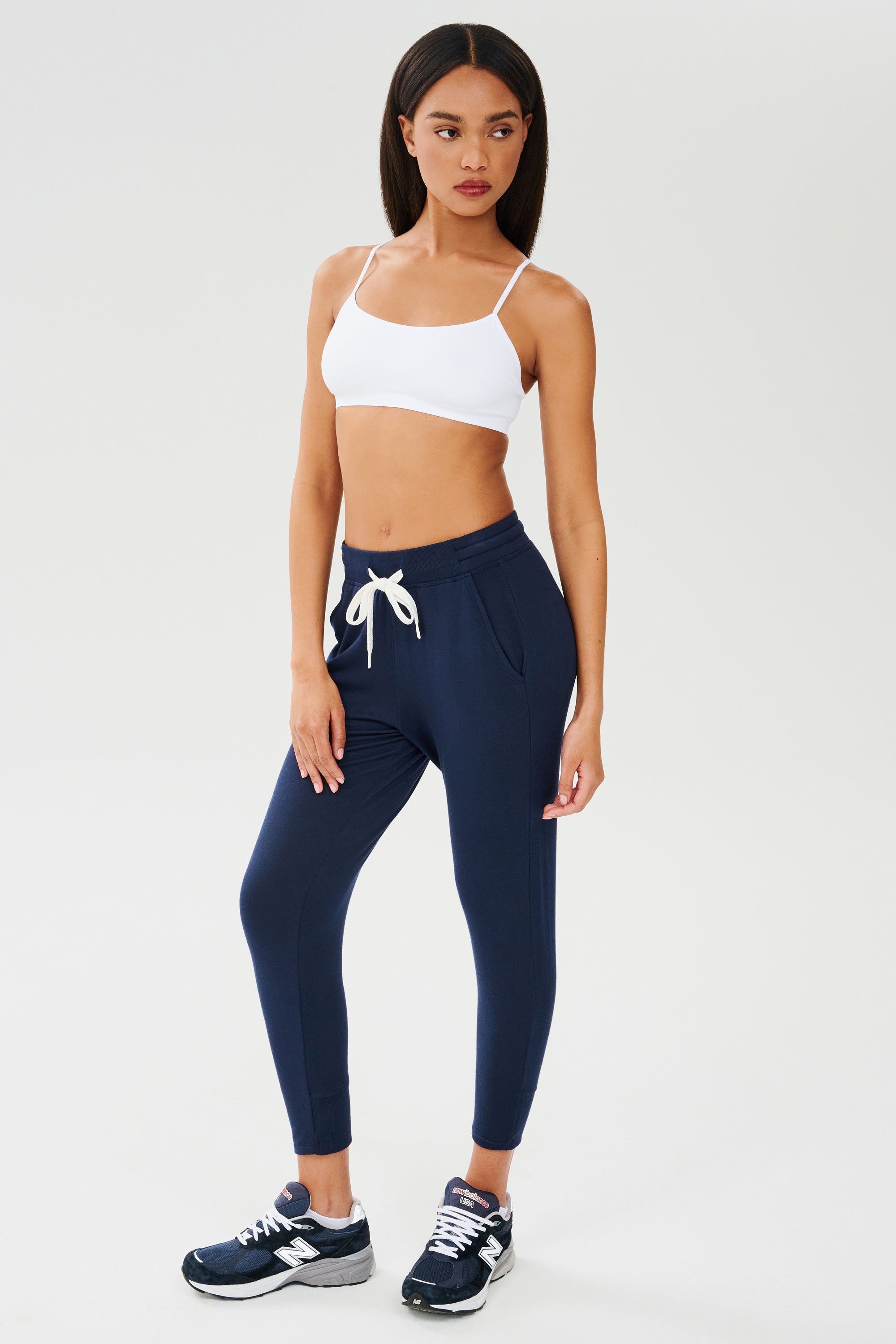 The model is wearing a Splits59 Loren Seamless Bra in white and navy sweatpants.