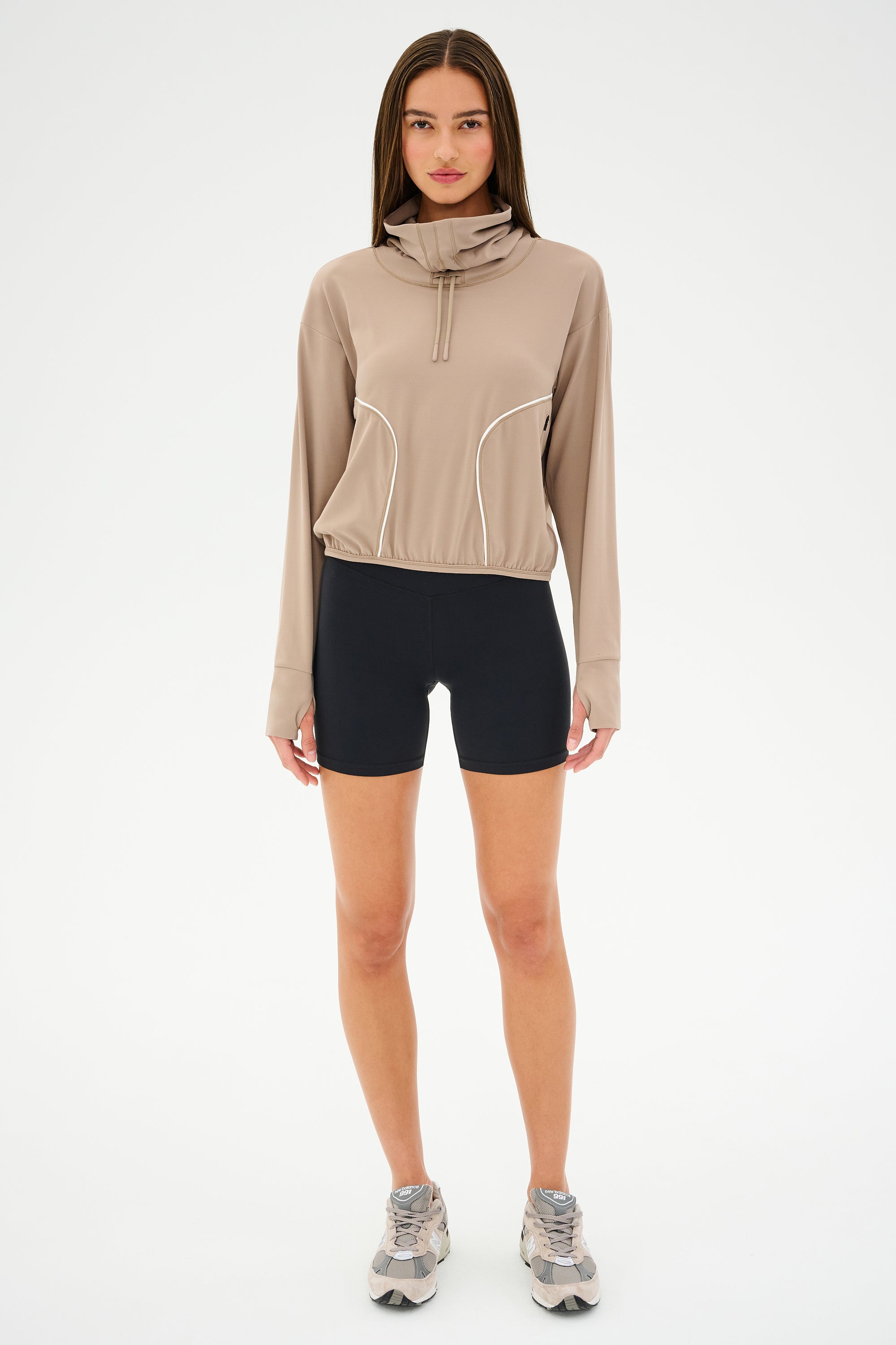 A person in a buttery soft SPLITS59 Rosie Airweight Jacket - Latte and black shorts stands on a white background, ready for hot yoga.