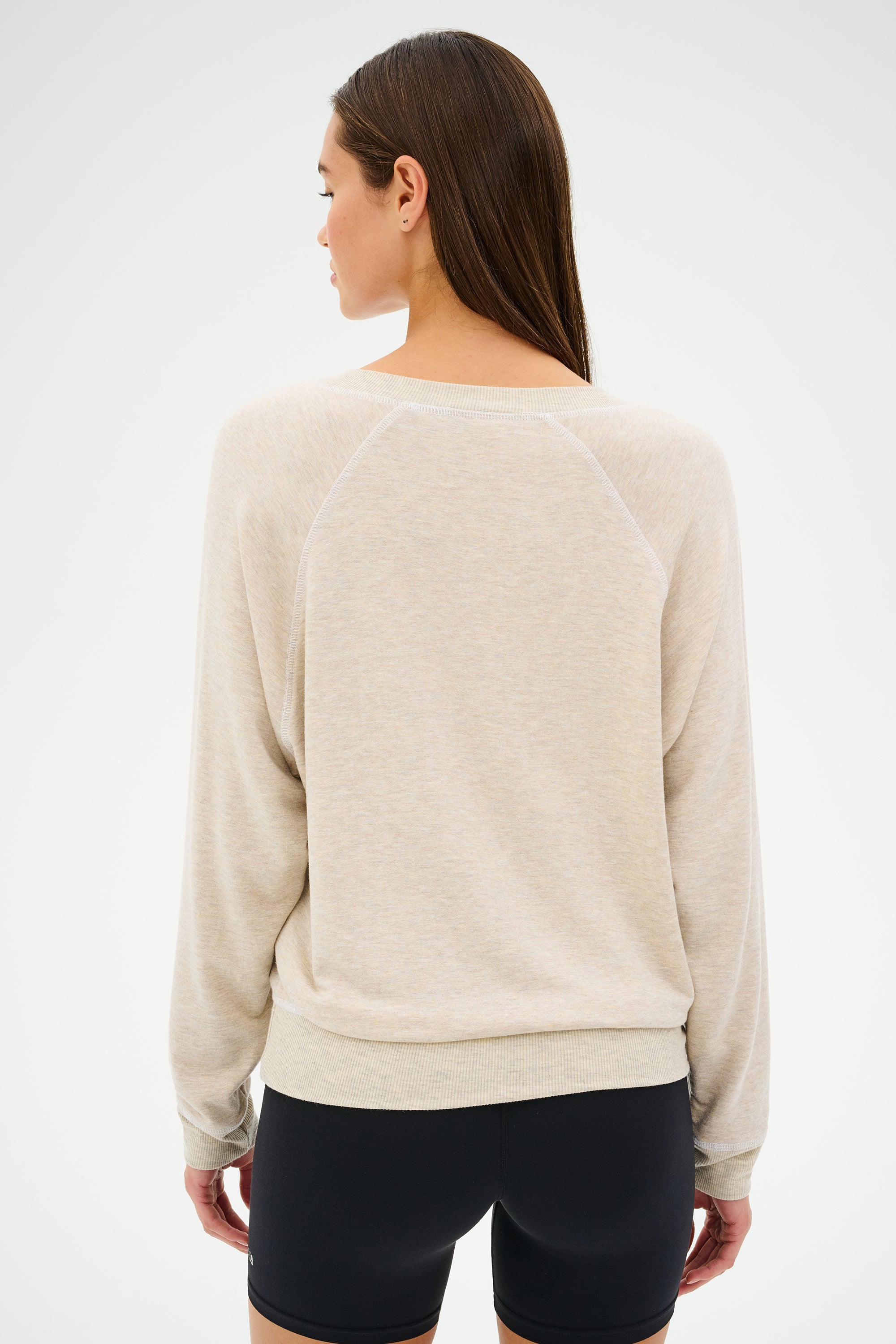 A person with long hair is wearing a SPLITS59 Bennie Fleece V-Neck Sweatshirt in Heather Oatmeal/White and black shorts, viewed from the back against a plain background.