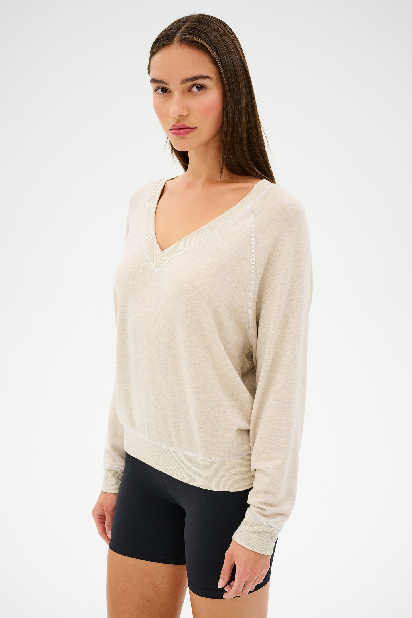 A person wears a SPLITS59 Bennie Fleece V-Neck Sweatshirt in Heather Oatmeal/White and black shorts, standing against a plain white background.