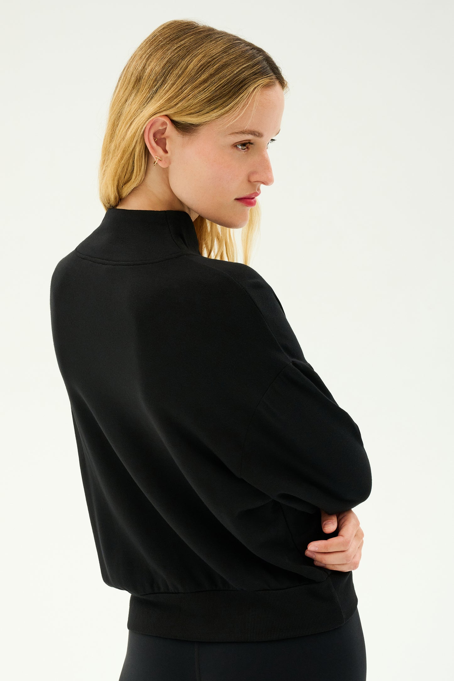 Side profile of a person with long blonde hair, wearing the SPLITS59 Birdie Fleece Half Zip in black, standing against a plain white background.