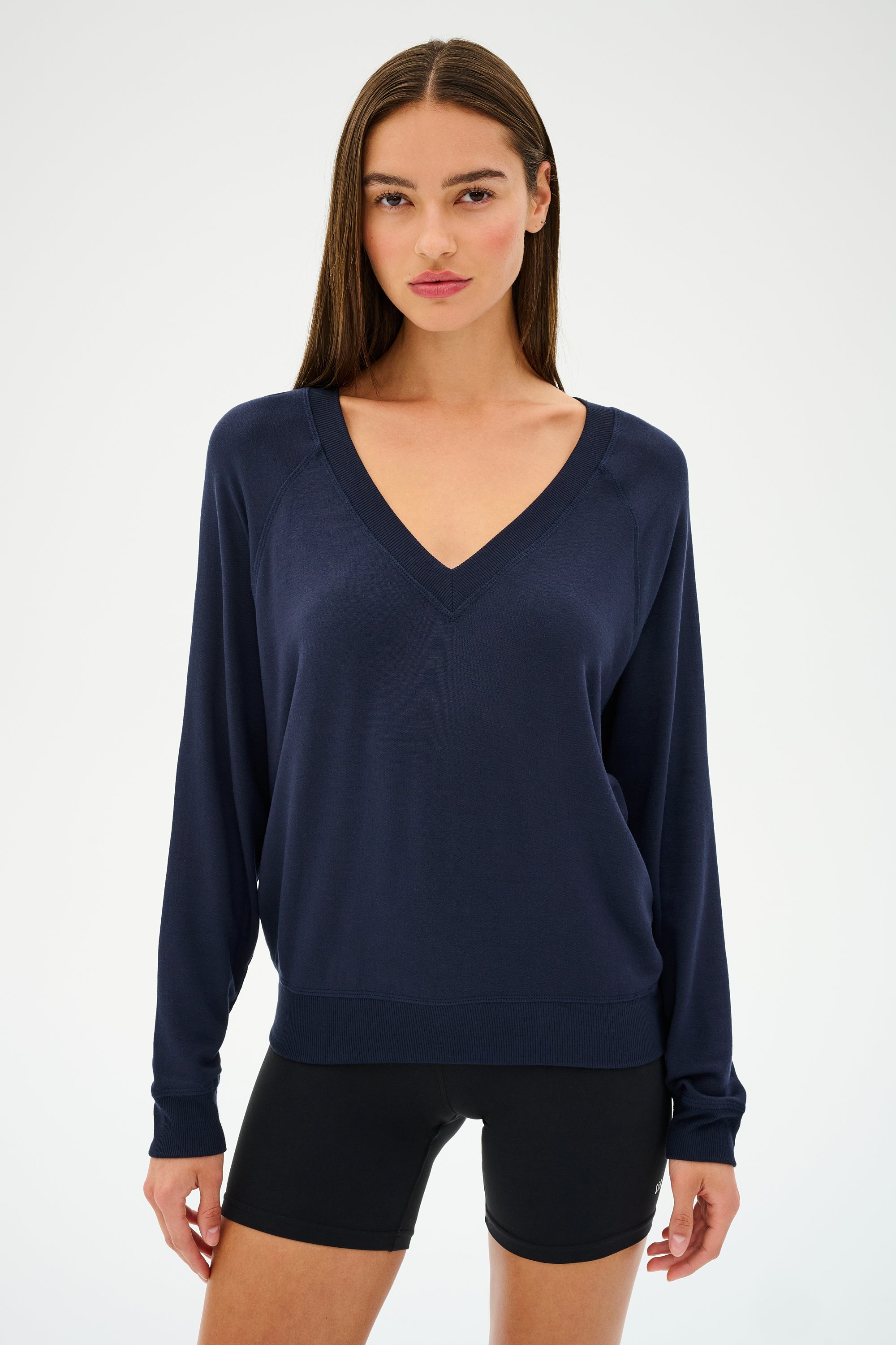 A person wearing the ultra-flattering Bennie Fleece V-Neck Sweatshirt in Indigo by SPLITS59, made in Los Angeles, stands against a plain background. The sweatshirt perfectly complements their black shorts.