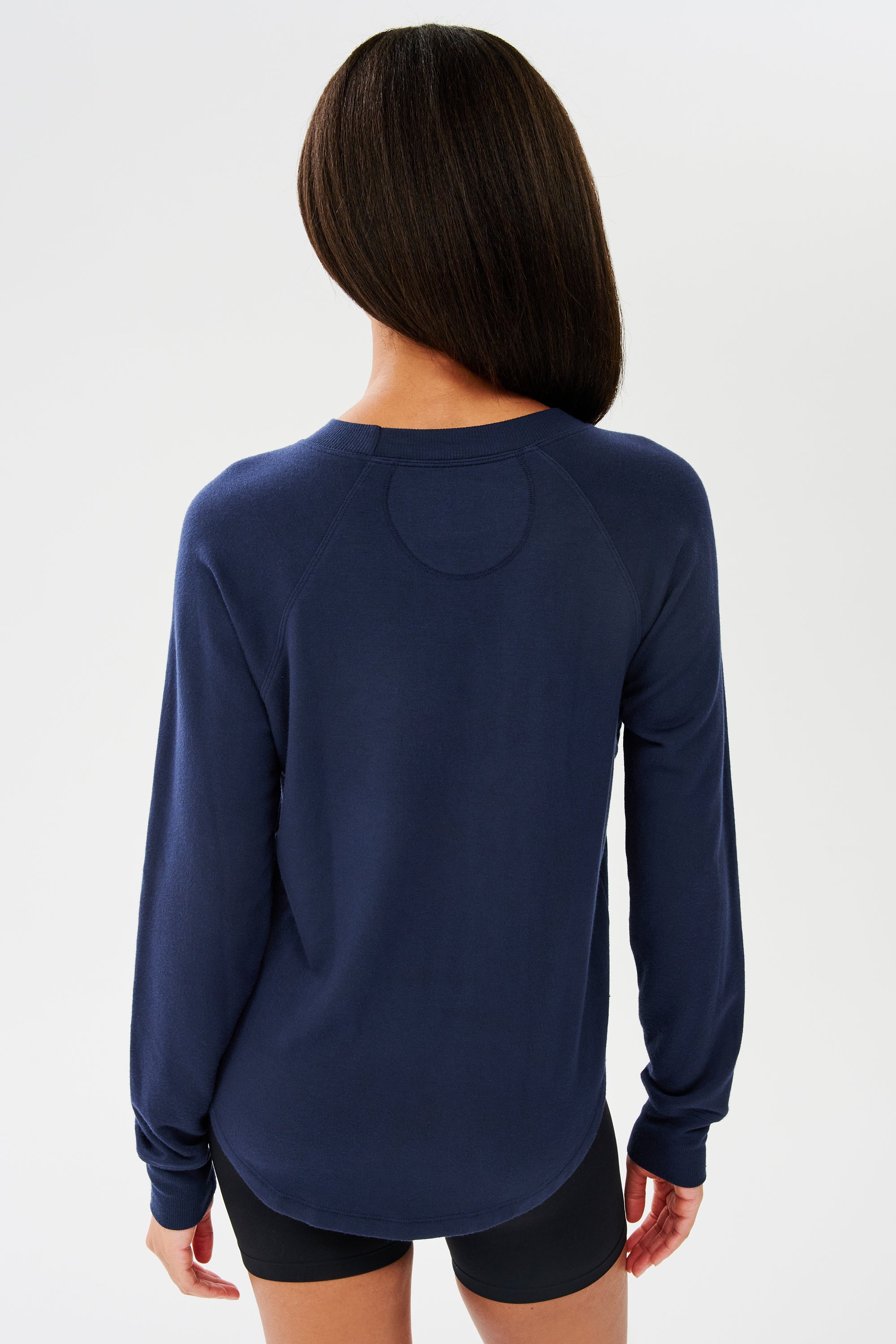 Back shot of woman with dark straight hair, wearing dark blue sweatshirt with black shorts 