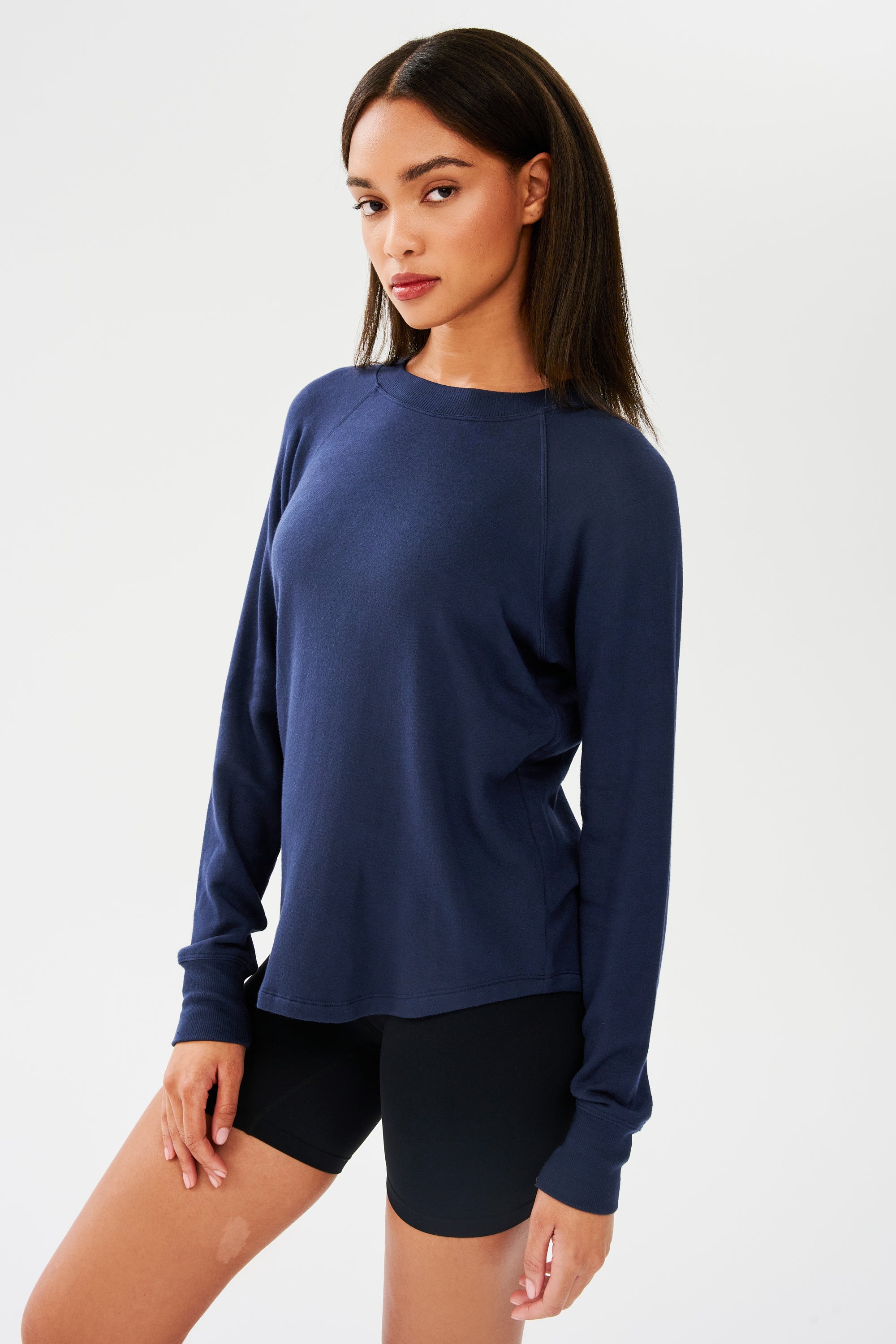 Side shot of woman with dark straight hair, wearing dark blue sweatshirt with black shorts 