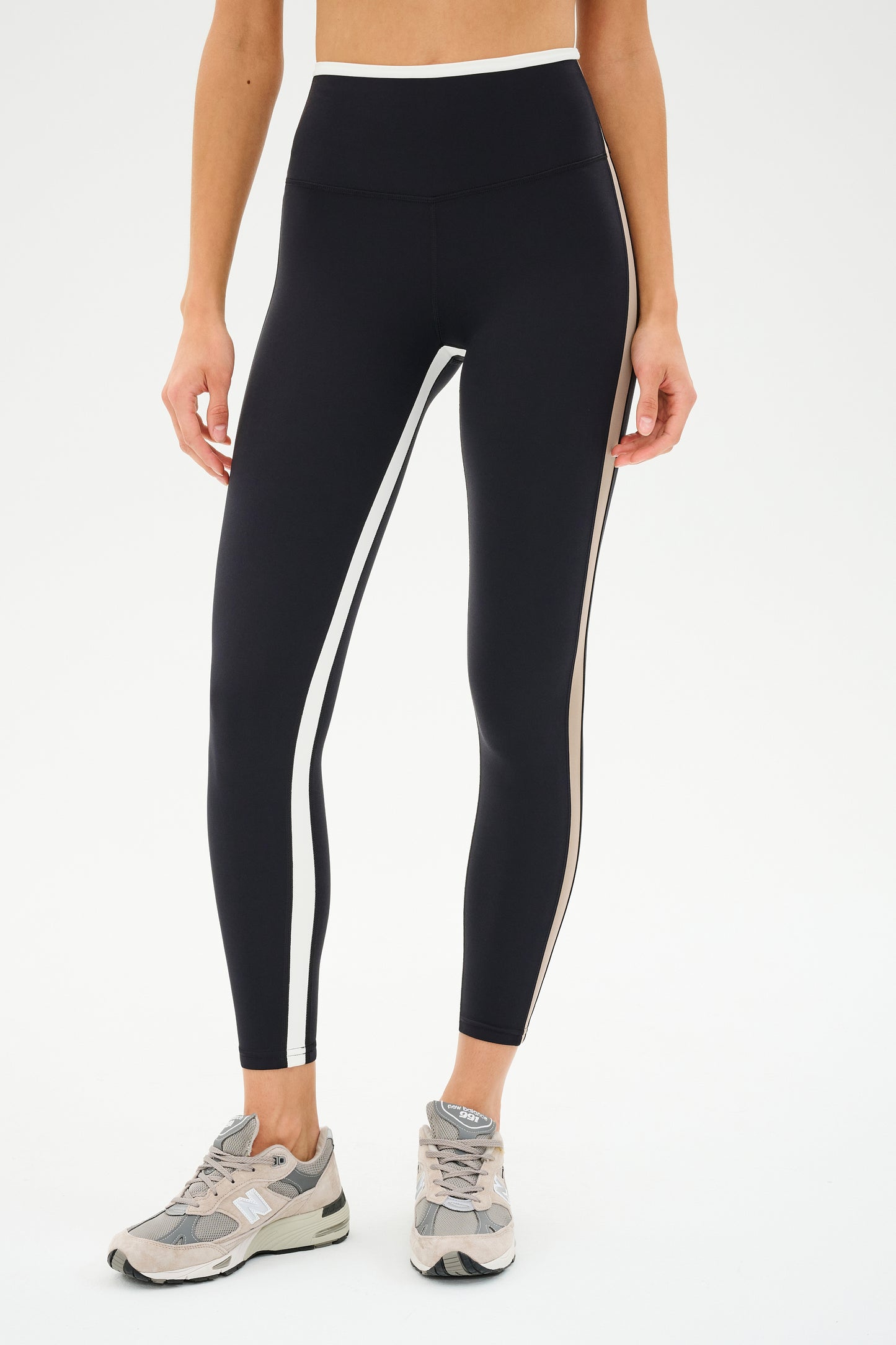 A person wearing SPLITS59 Sam High Waist Rigor 7/8 leggings in Black/Latte and gray sneakers stands against a white background.