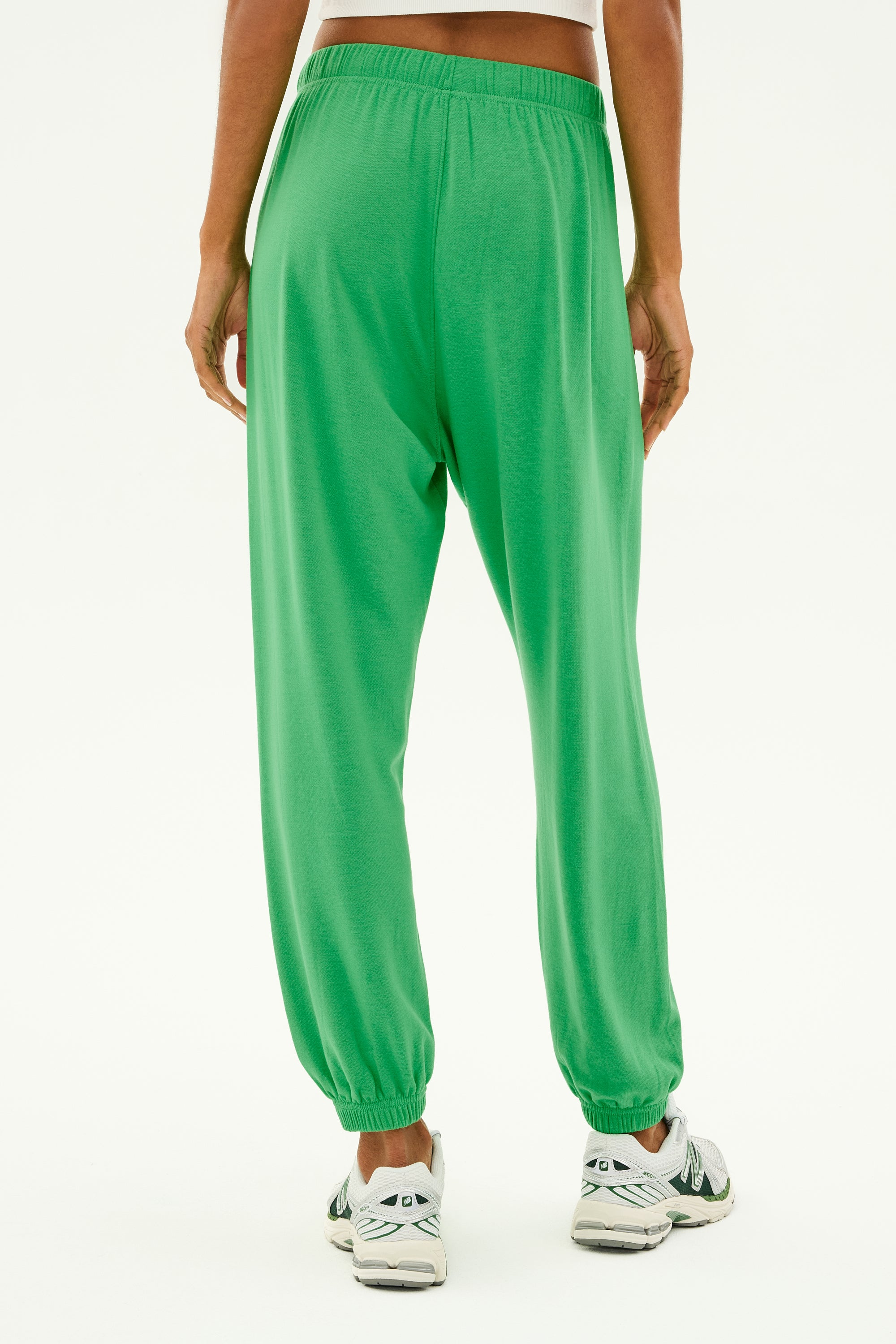 A person is seen from the back wearing SPLITS59's Andie Oversized Fleece Sweatpant in Grass, ideal for workouts in cool weather, paired with white sneakers against a plain background.