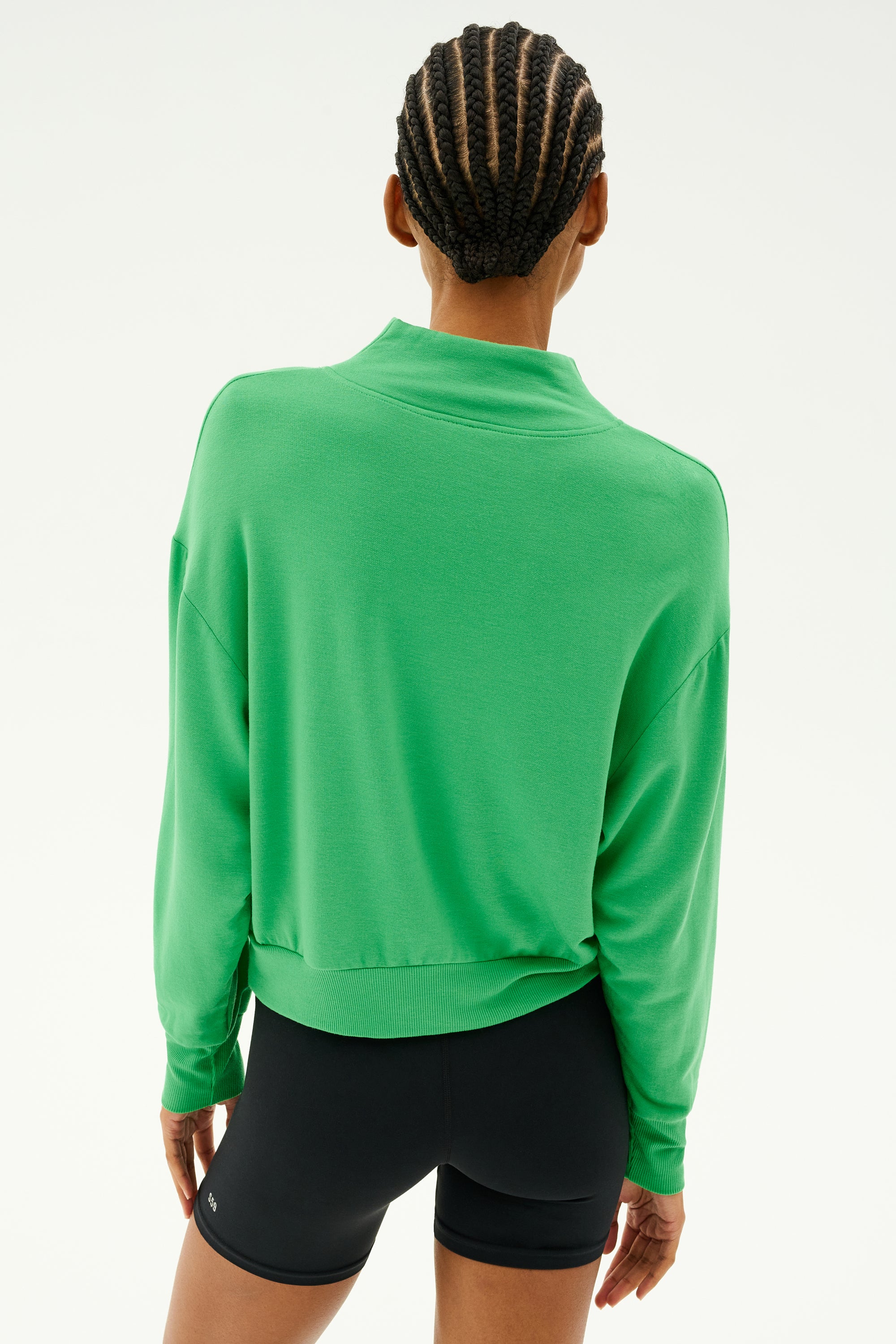 A person wearing the Birdie Fleece Half Zip in Grass by SPLITS59, paired with black shorts, is shown from the back against a plain background, ideal for winter workouts.