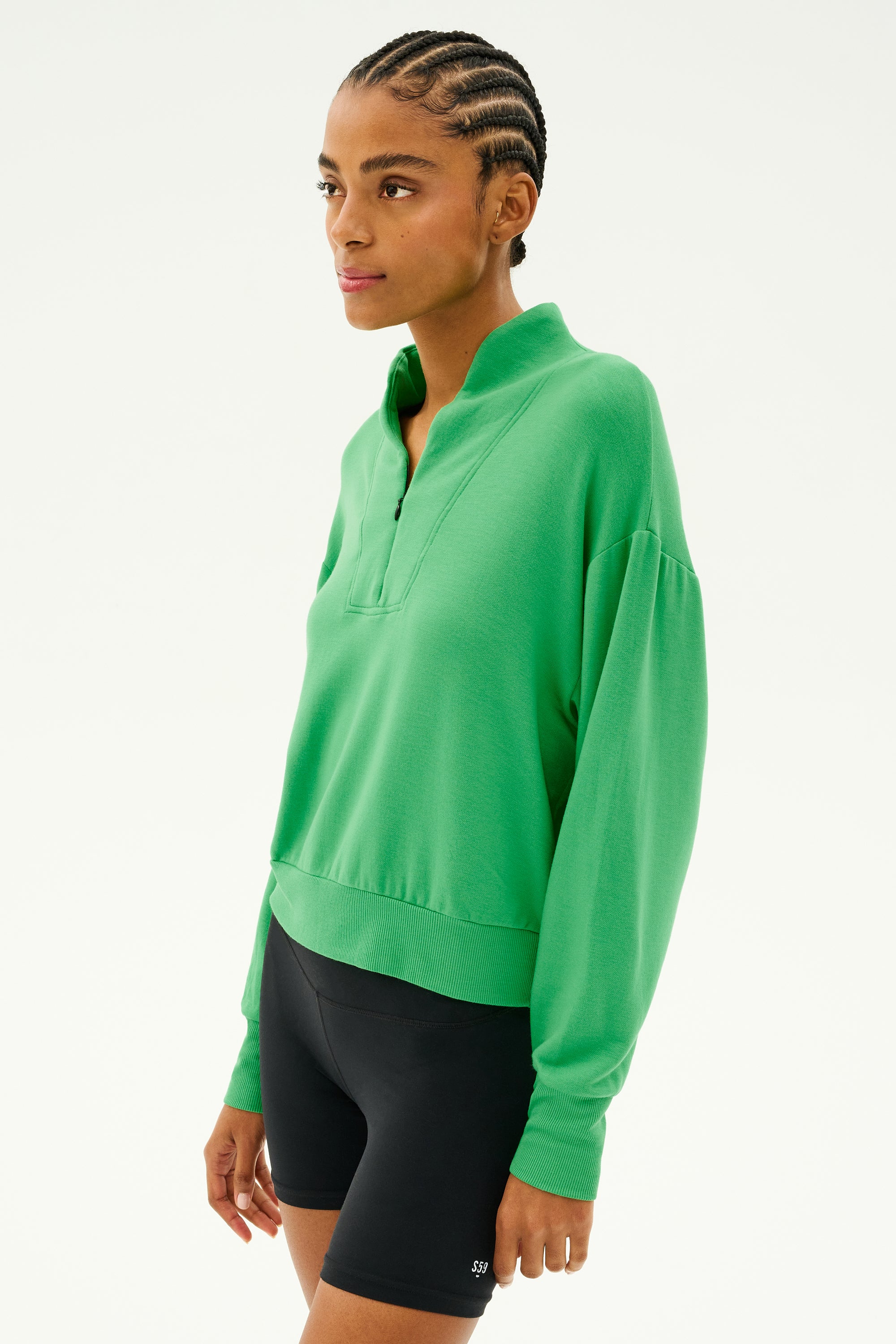 A person wearing the Birdie Fleece Half Zip - Grass by SPLITS59 and black shorts, ideal for winter workouts, stands against a plain background.