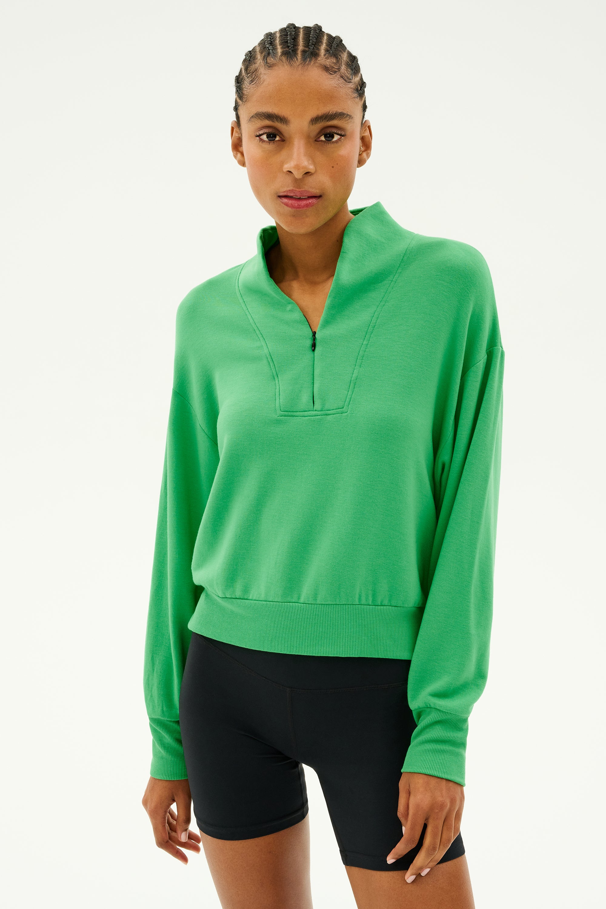 A person dressed in the SPLITS59 Birdie Fleece Half Zip in Grass and black shorts stands against a simple background, prepared for winter workouts.