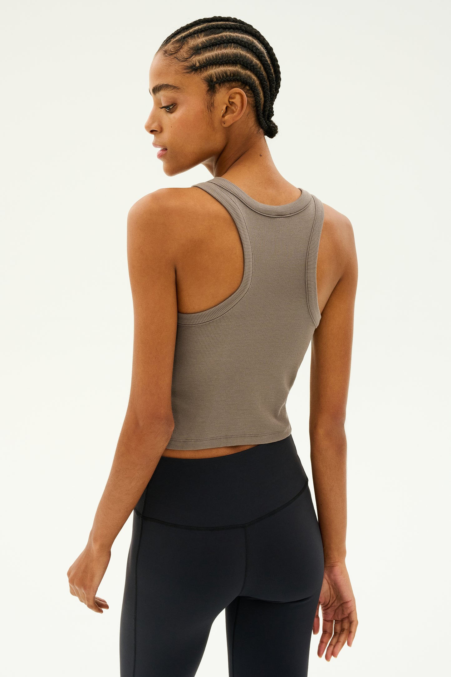 A person wearing the Kiki Rib Crop - Lentil from SPLITS59, crafted from soft baby rib fabric and paired with black leggings, stands facing sideways against a plain background. MADE IN LOS ANGELES.