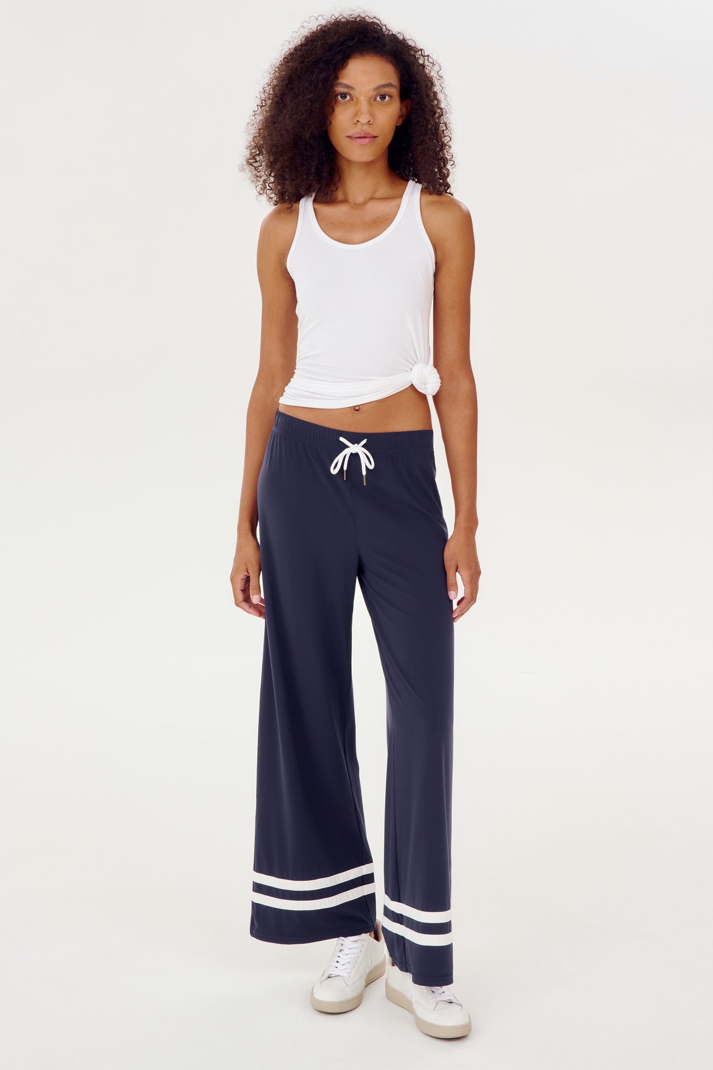 A woman wearing a white tank top and SPLITS59's Quinn Airweight Wide Leg Pant in Indigo, perfect for a comfortable yoga session.