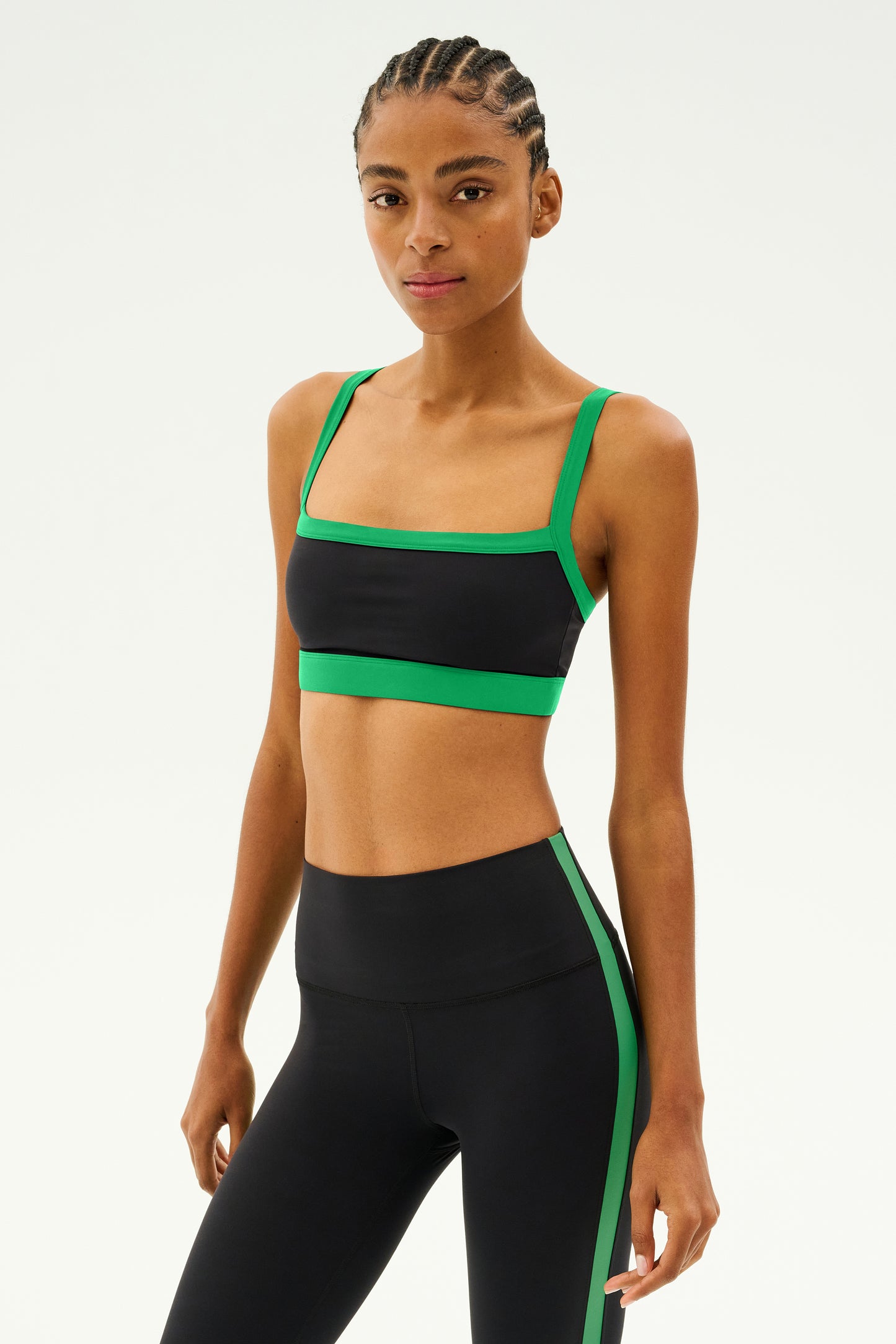 A person wearing the SPLITS59 Monah Rigor Bra in black and grass, a sleek athletic outfit made of stretchy spandex, stands against a plain background.