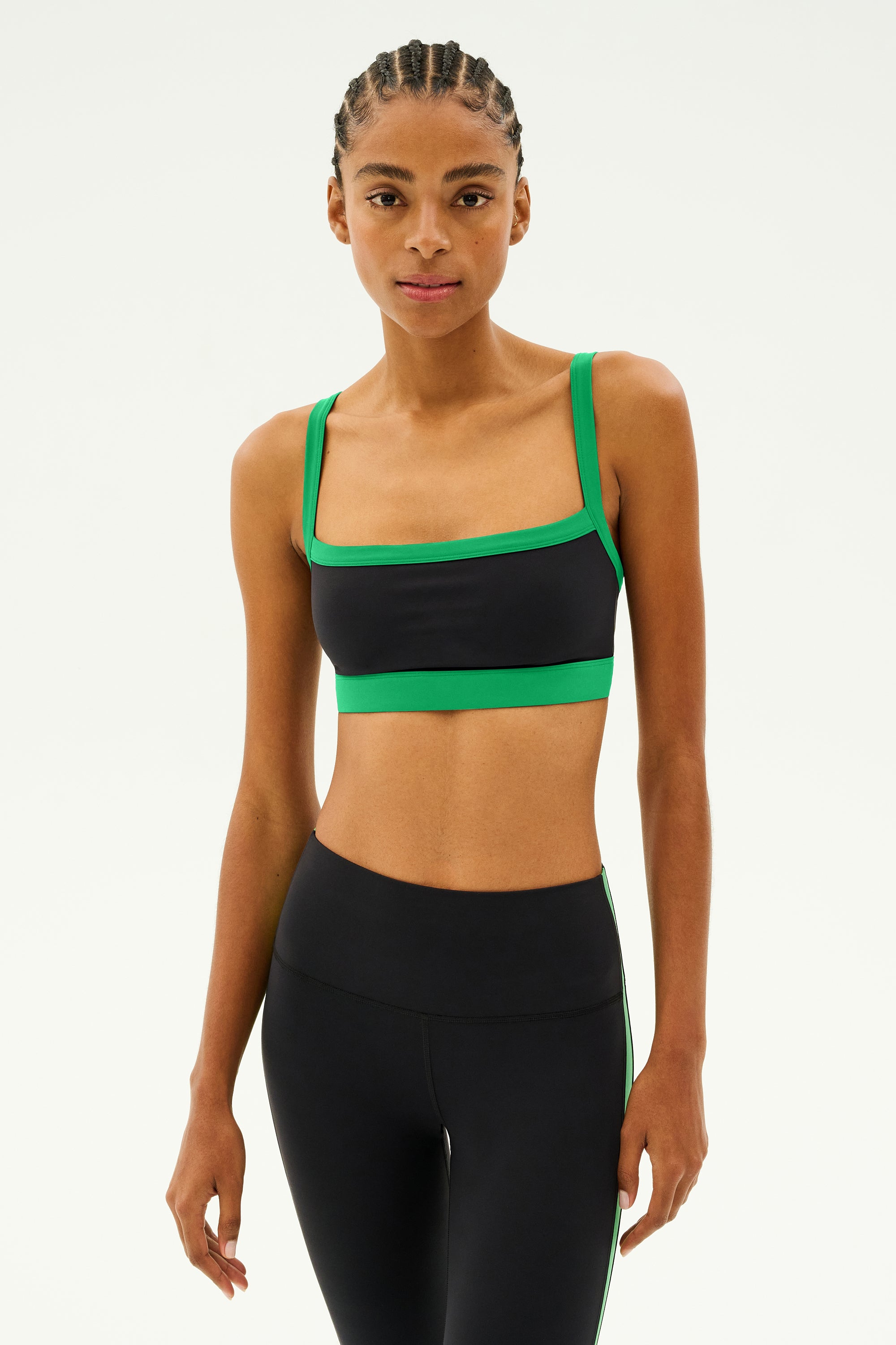 A person wearing the Monah Rigor Bra in black and grass from SPLITS59 sports a sleek spandex ensemble against a plain background.