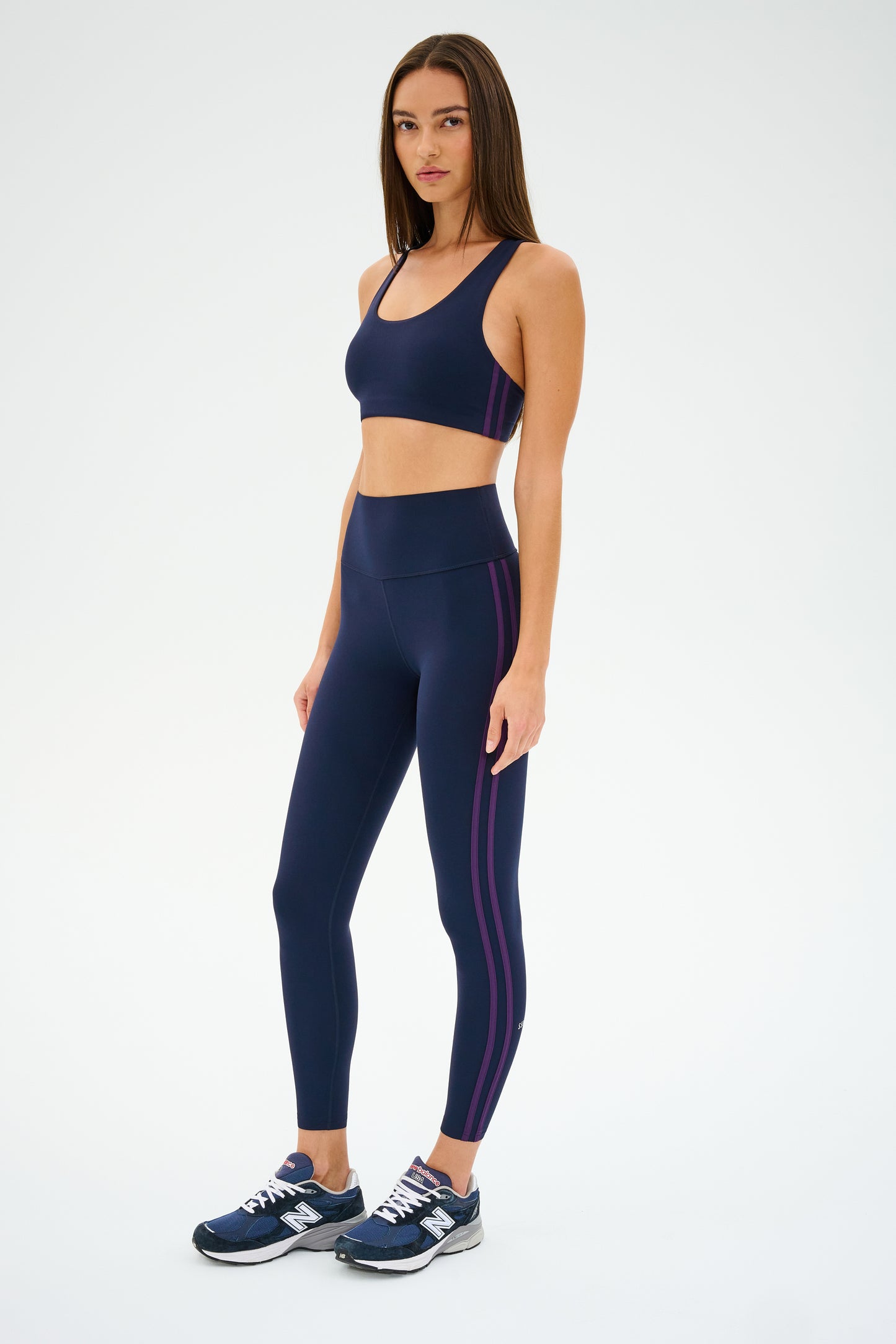 In SPLITS59's Ella Airweight Bra in Indigo/Black Currant, a person stands against a plain background wearing lightweight sneakers, perfect for hot yoga.