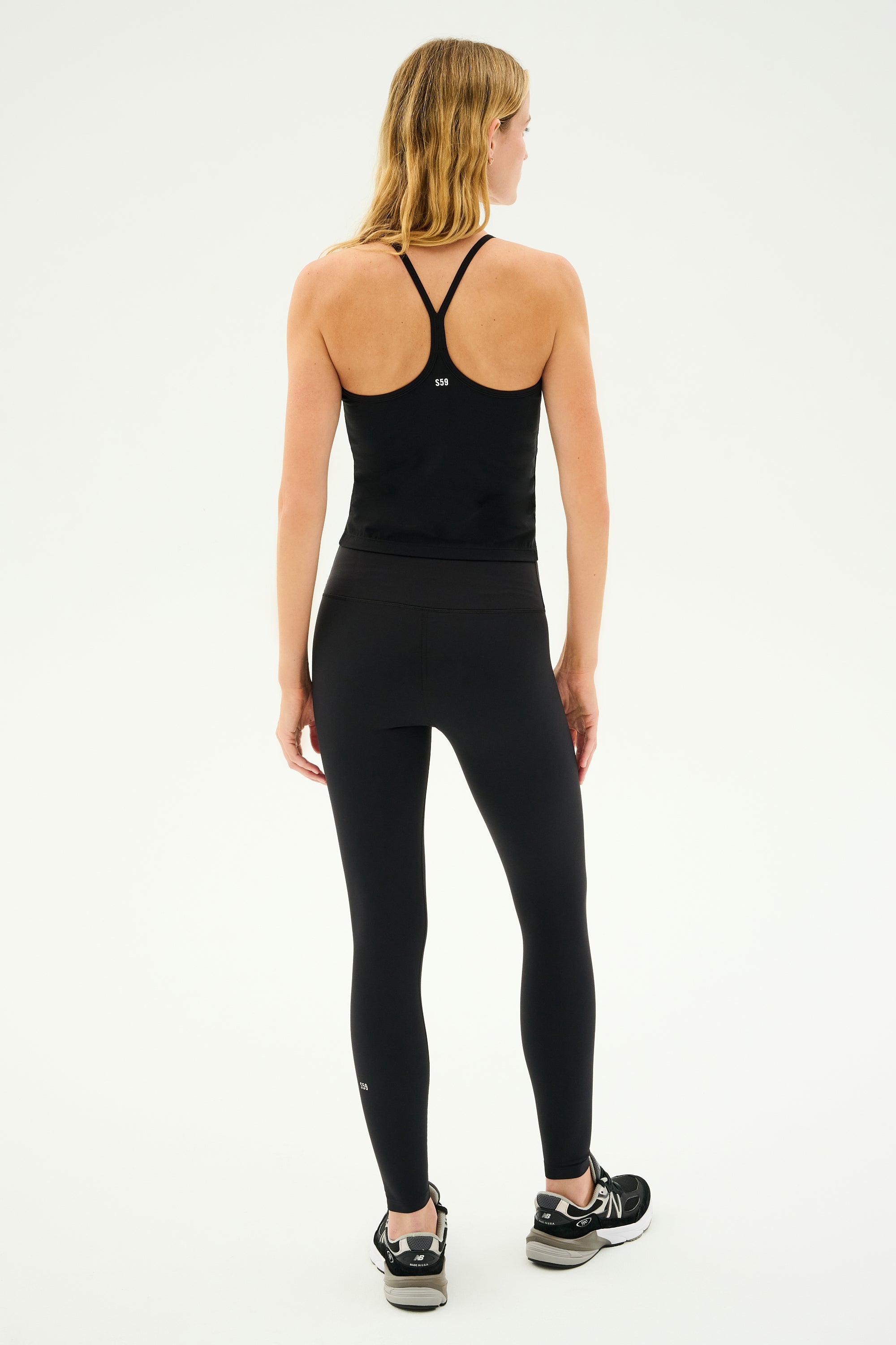 A person is seen from behind wearing the SPLITS59 Airweight Tank in black athletic wear, standing against a plain background in sneakers.