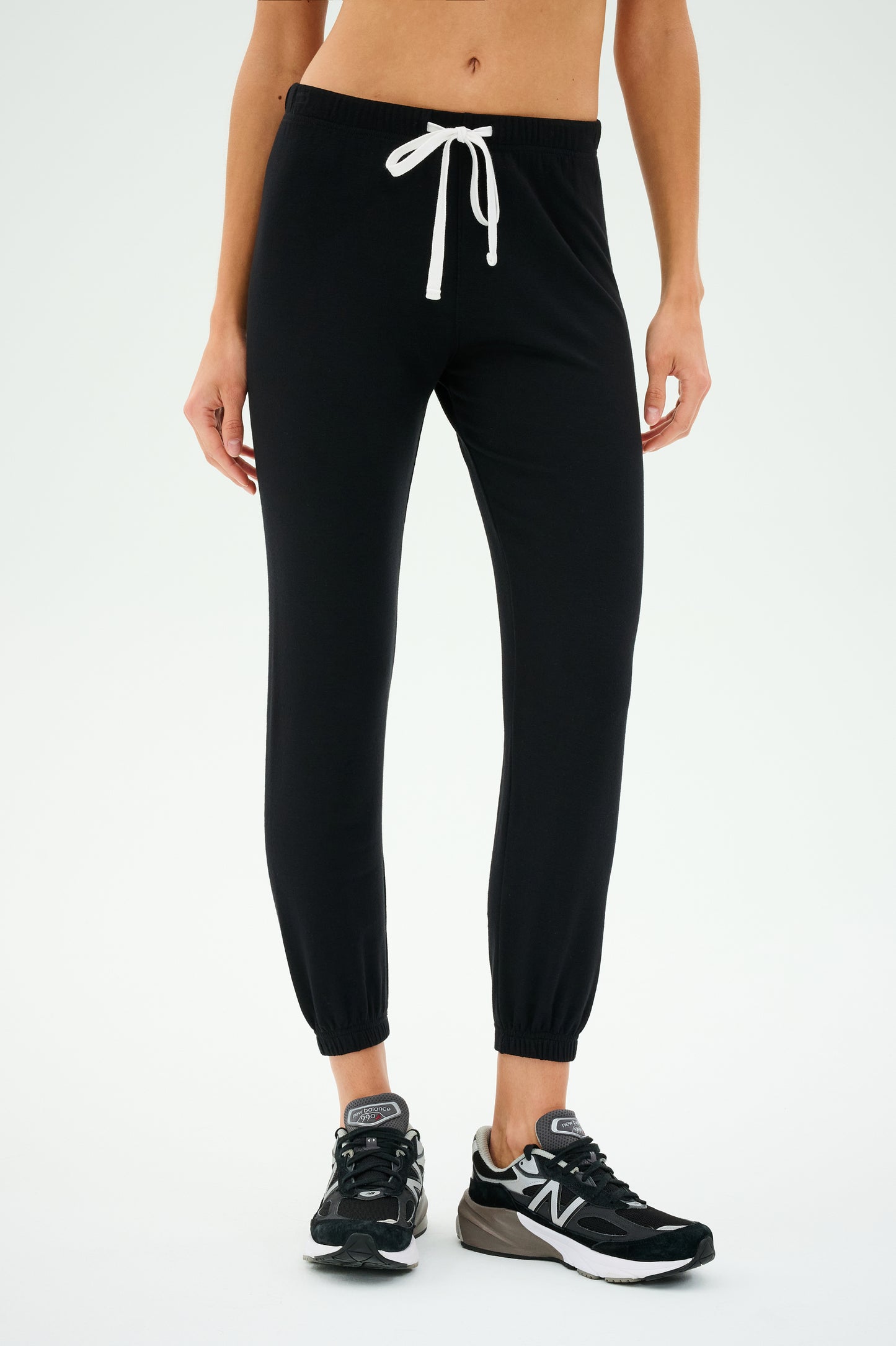 A person wearing SPLITS59 Sonja Fleece Sweatpant in black with a white drawstring, paired with black sneakers, ready for workouts.