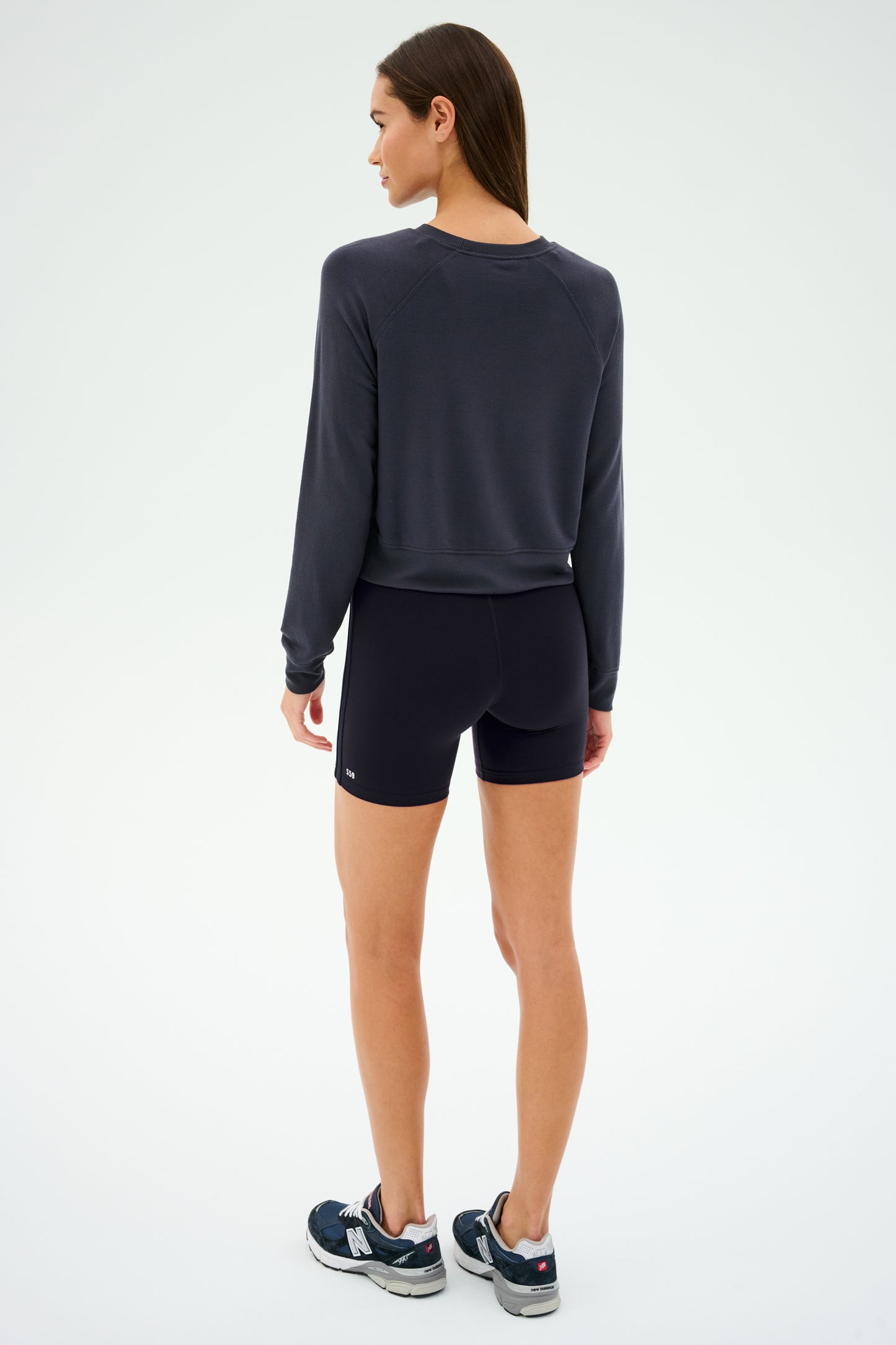 Facing away in a graphite, semi-cropped Brooks fleece long sleeve sweatshirt by SPLITS59 and black shorts, a person stands in sneakers against a plain background. The pullover subtly features "MADE IN LOS ANGELES" across the back.