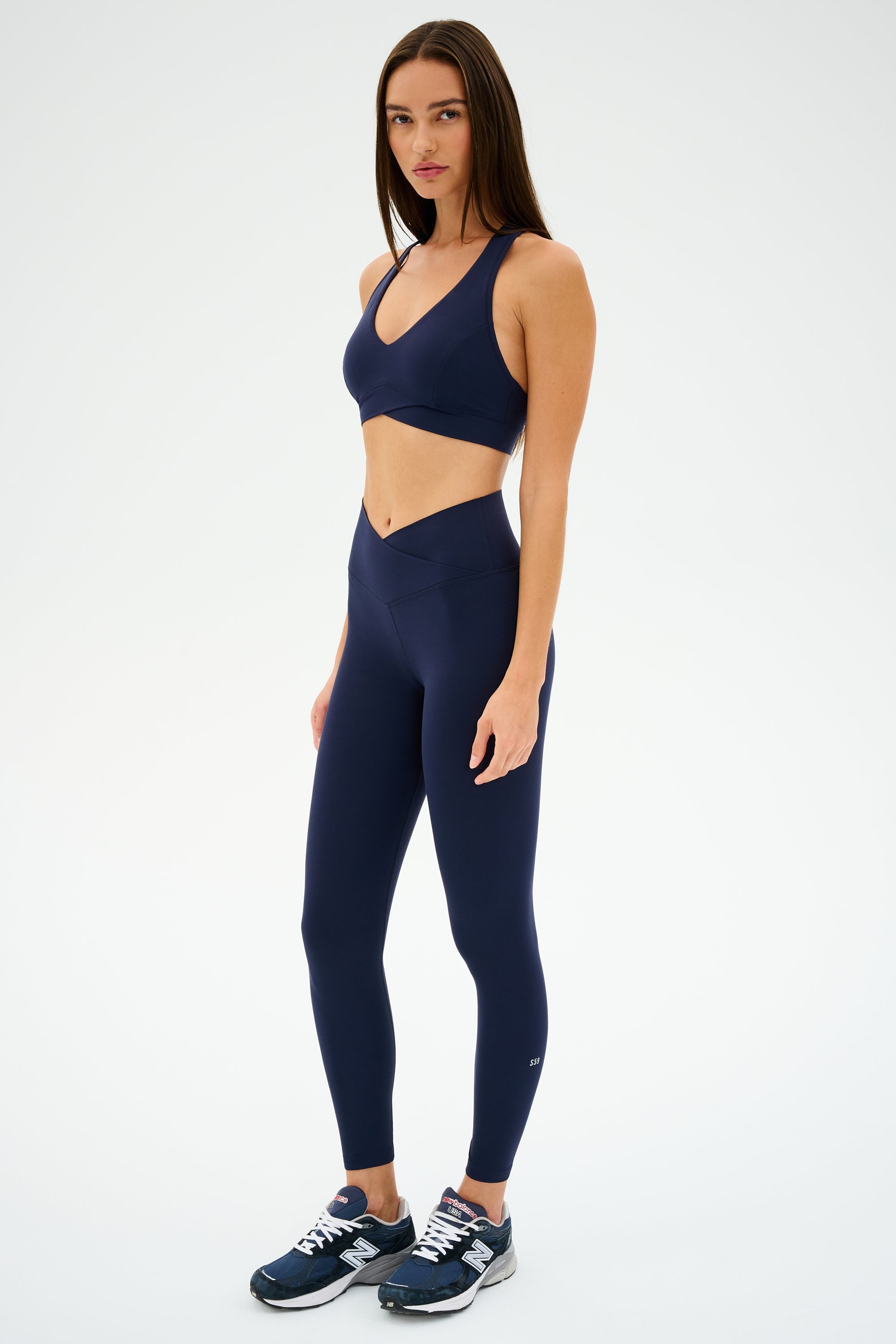 A person in the matching Mia Rigor 7/8 - Indigo set by SPLITS59, with sneakers, stands against a white background, ready for workouts.