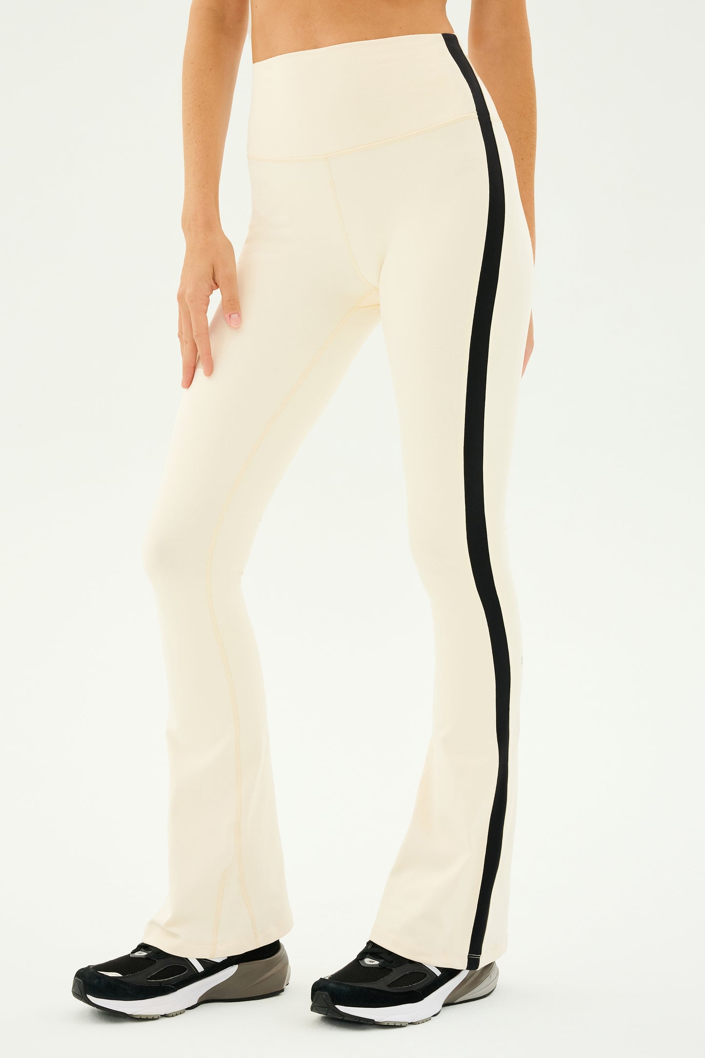 Someone dressed in the SPLITS59 Raquel High Waist Flared Legging in Creme/Black paired with black sneakers, ideal for yoga sessions or simply a fashionable day out.