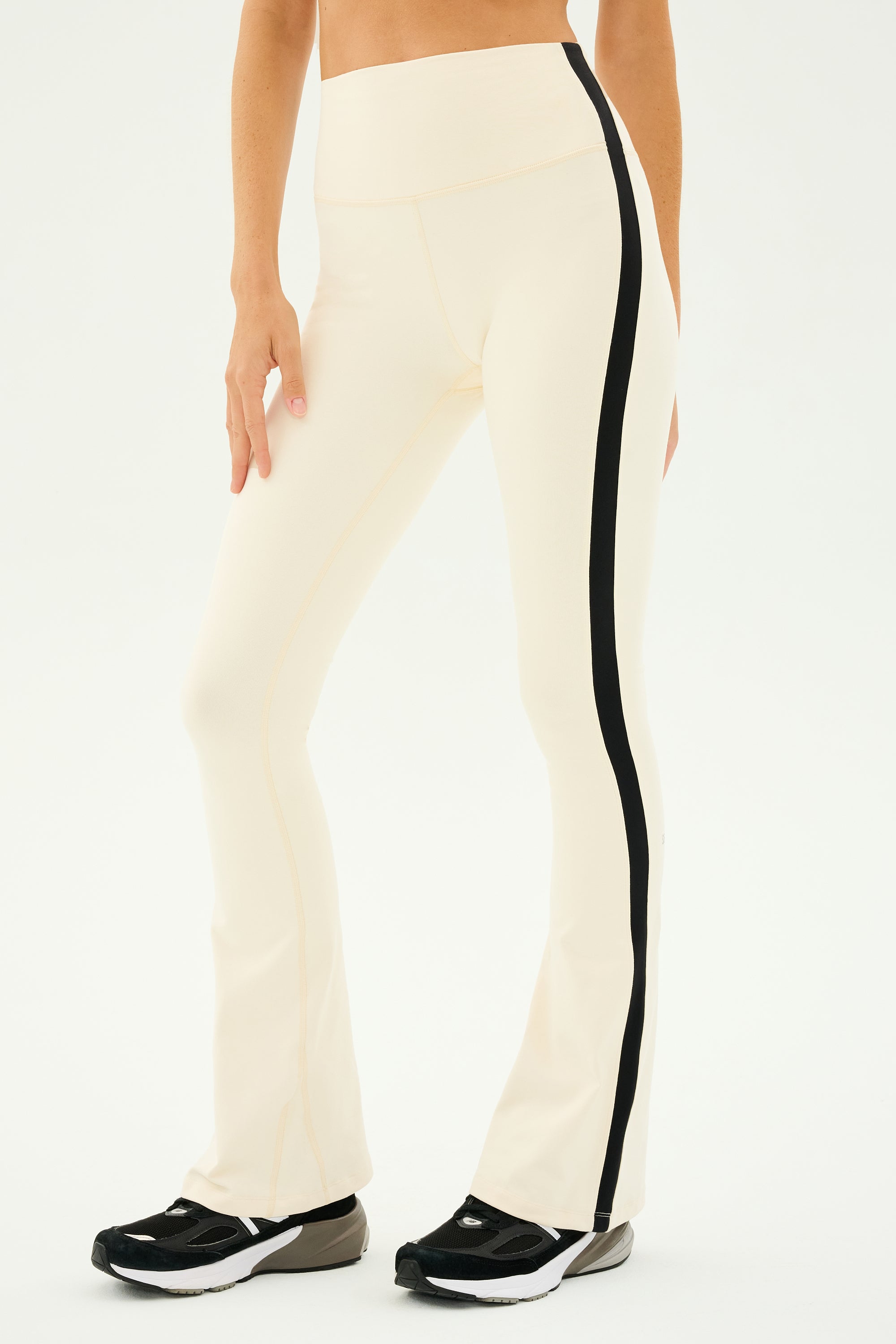 Someone dressed in the SPLITS59 Raquel High Waist Flared Legging in Creme/Black paired with black sneakers, ideal for yoga sessions or simply a fashionable day out.