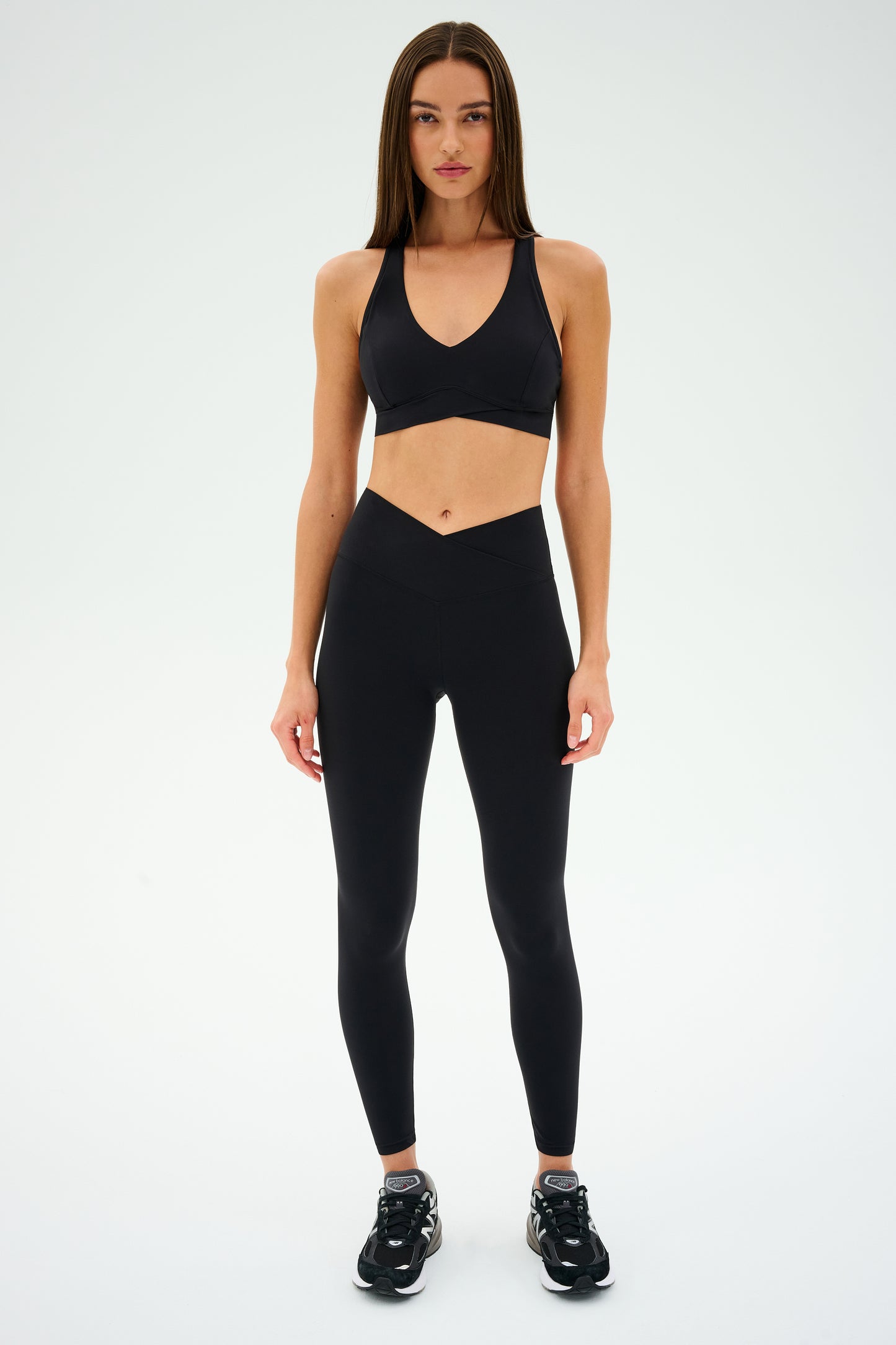 A woman models the Mia Rigor Bra by SPLITS59 paired with black leggings and sneakers against a neutral background.