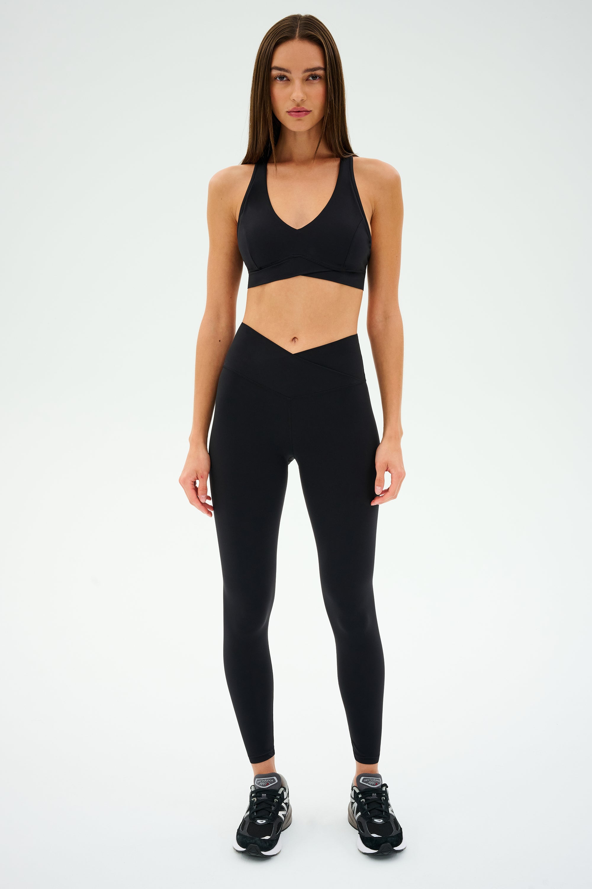 A woman models the Mia Rigor Bra by SPLITS59 paired with black leggings and sneakers against a neutral background.